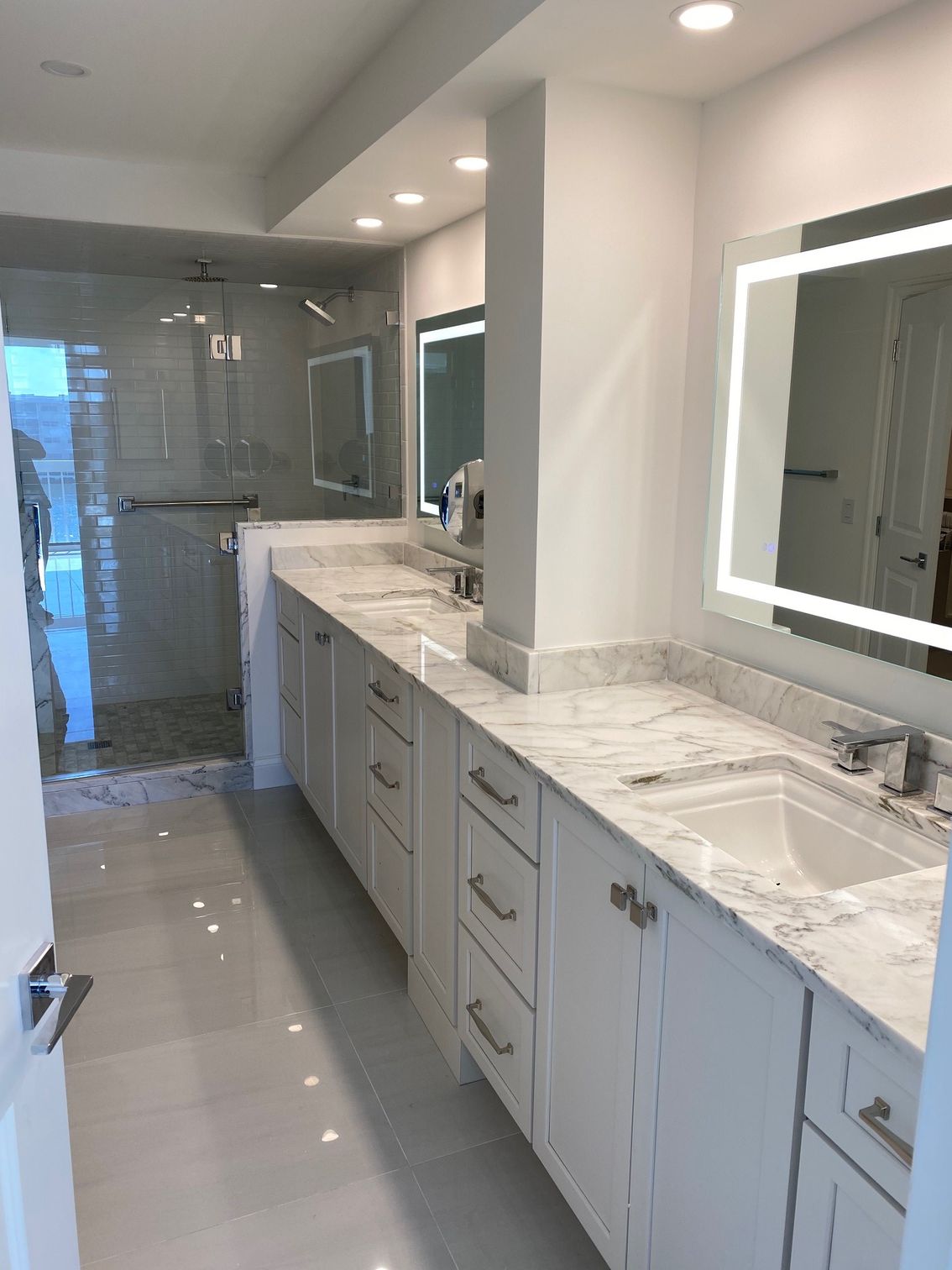 White modern bathroom with double vanity, marble countertops, and a glass-enclosed shower.