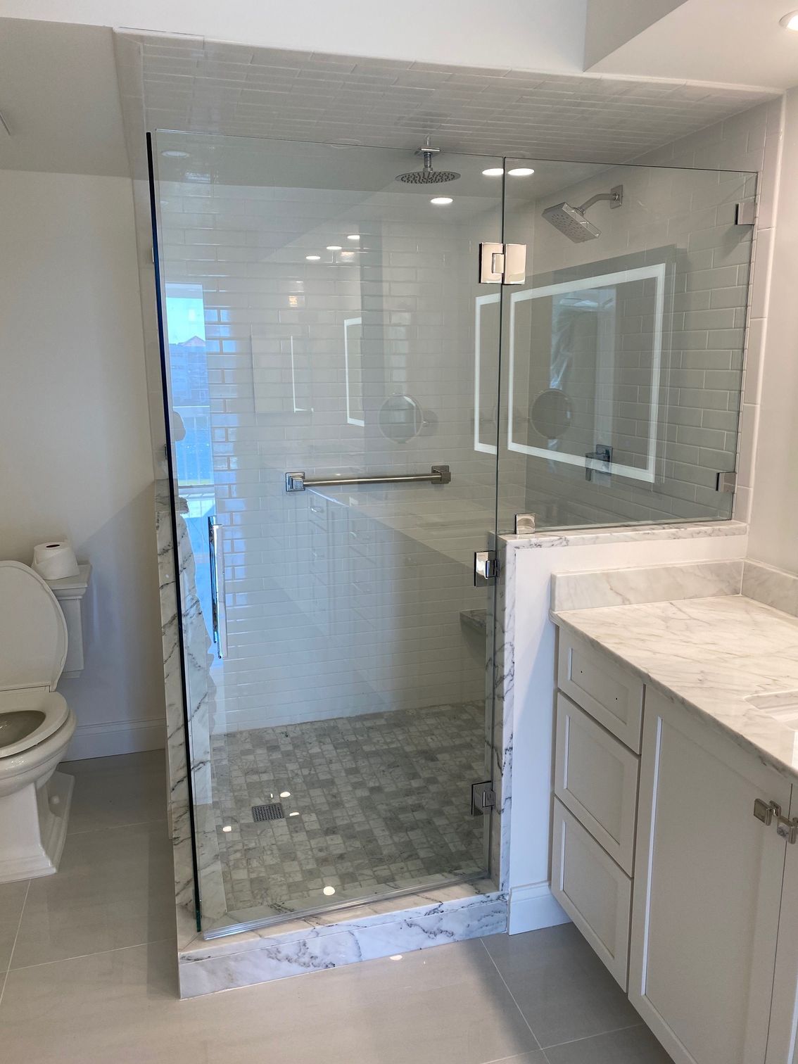 Bathroom with glass shower, white vanity, and toilet. Tile walls and floor.