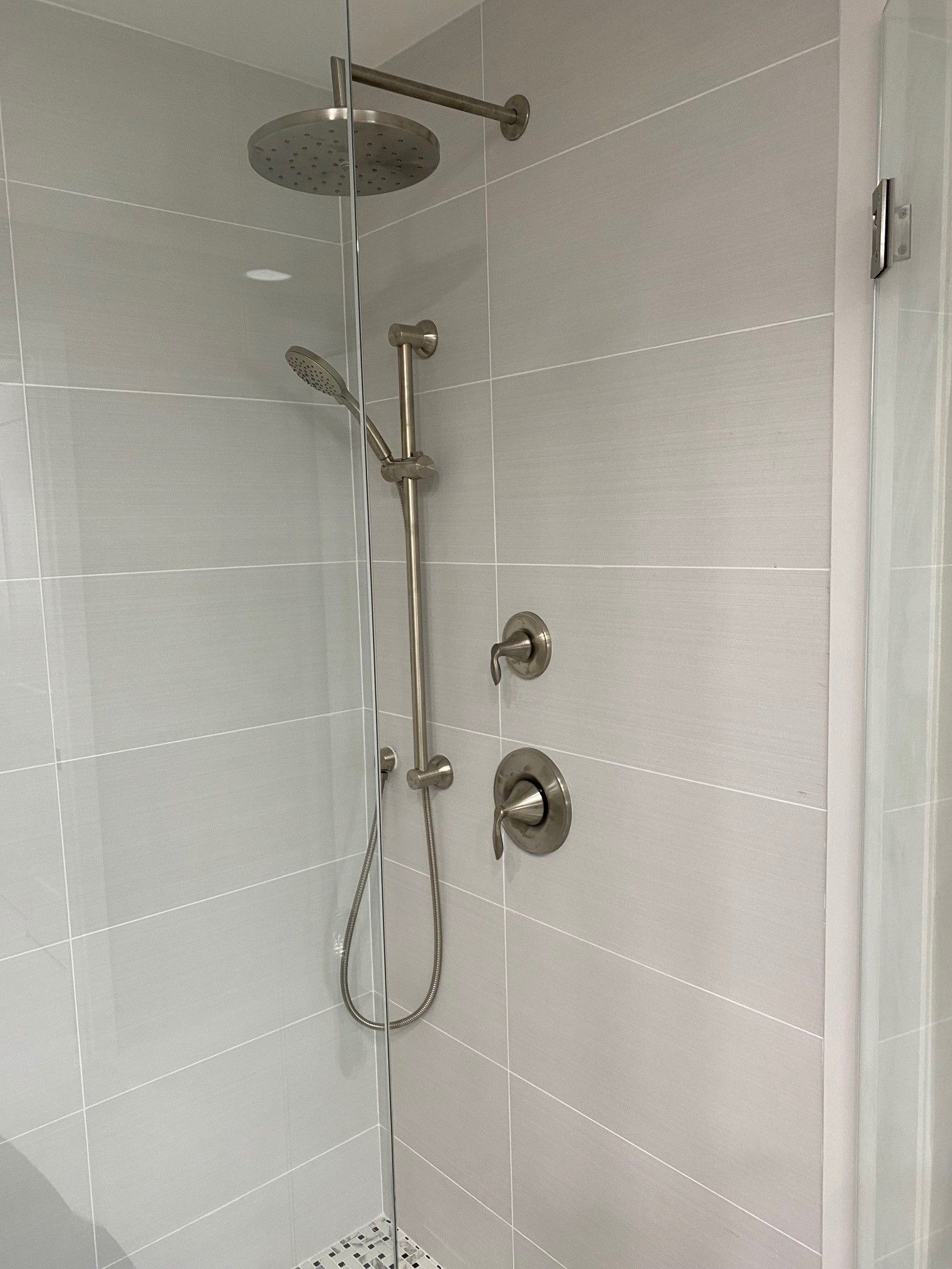 Modern shower with silver fixtures, including rain shower head and handheld sprayer, on white tiled wall.