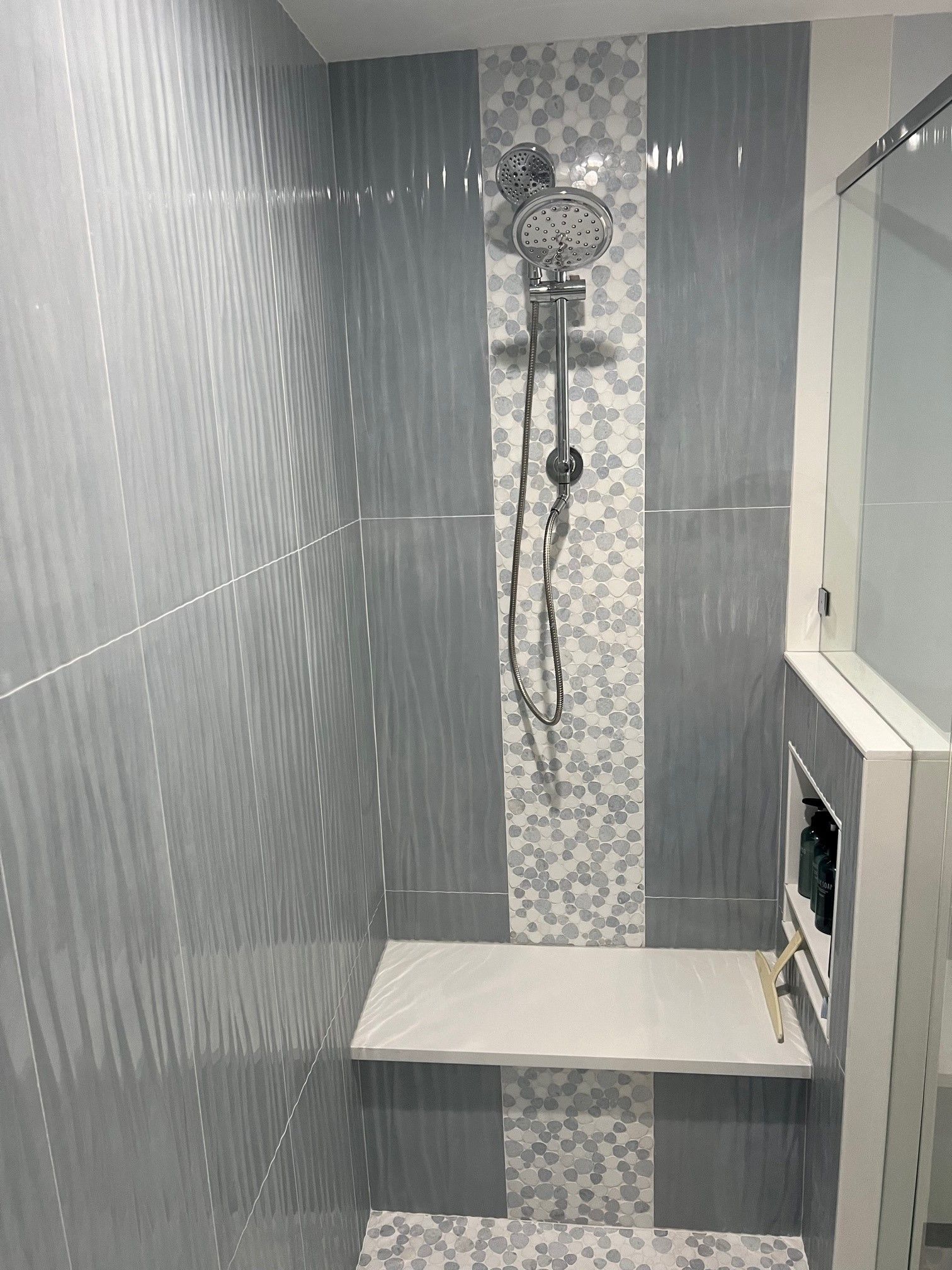 Gray and white tiled shower with built-in bench, central mosaic stripe, and showerhead.