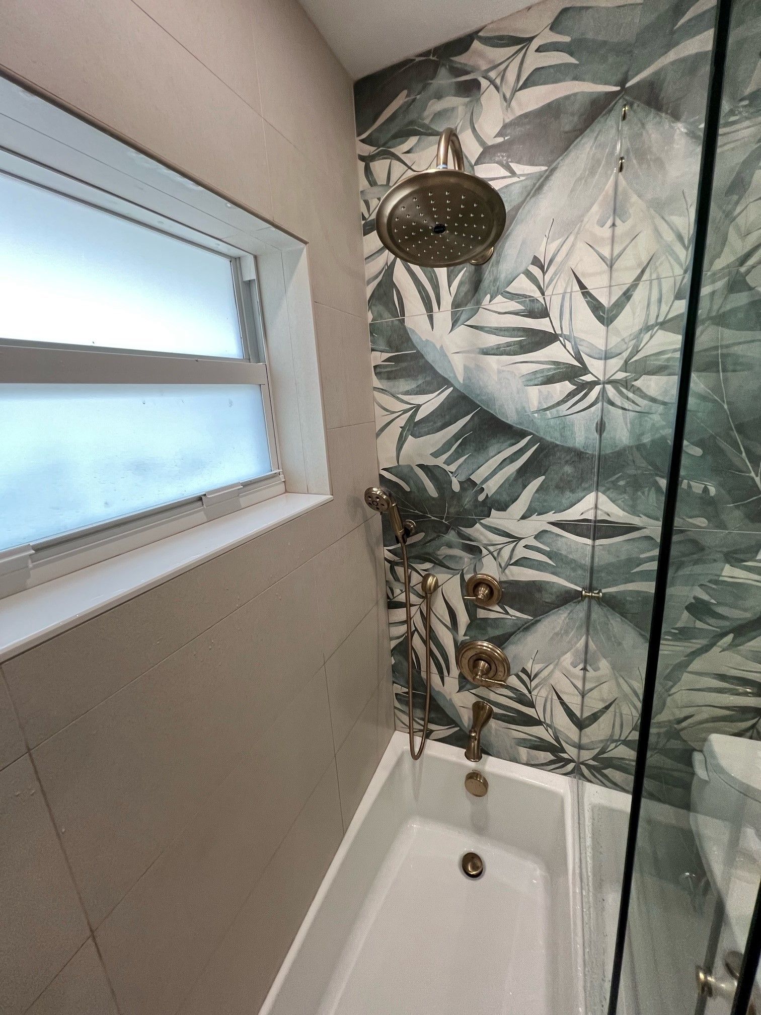 Bathroom with bathtub, shower head, decorative tile, and a window.