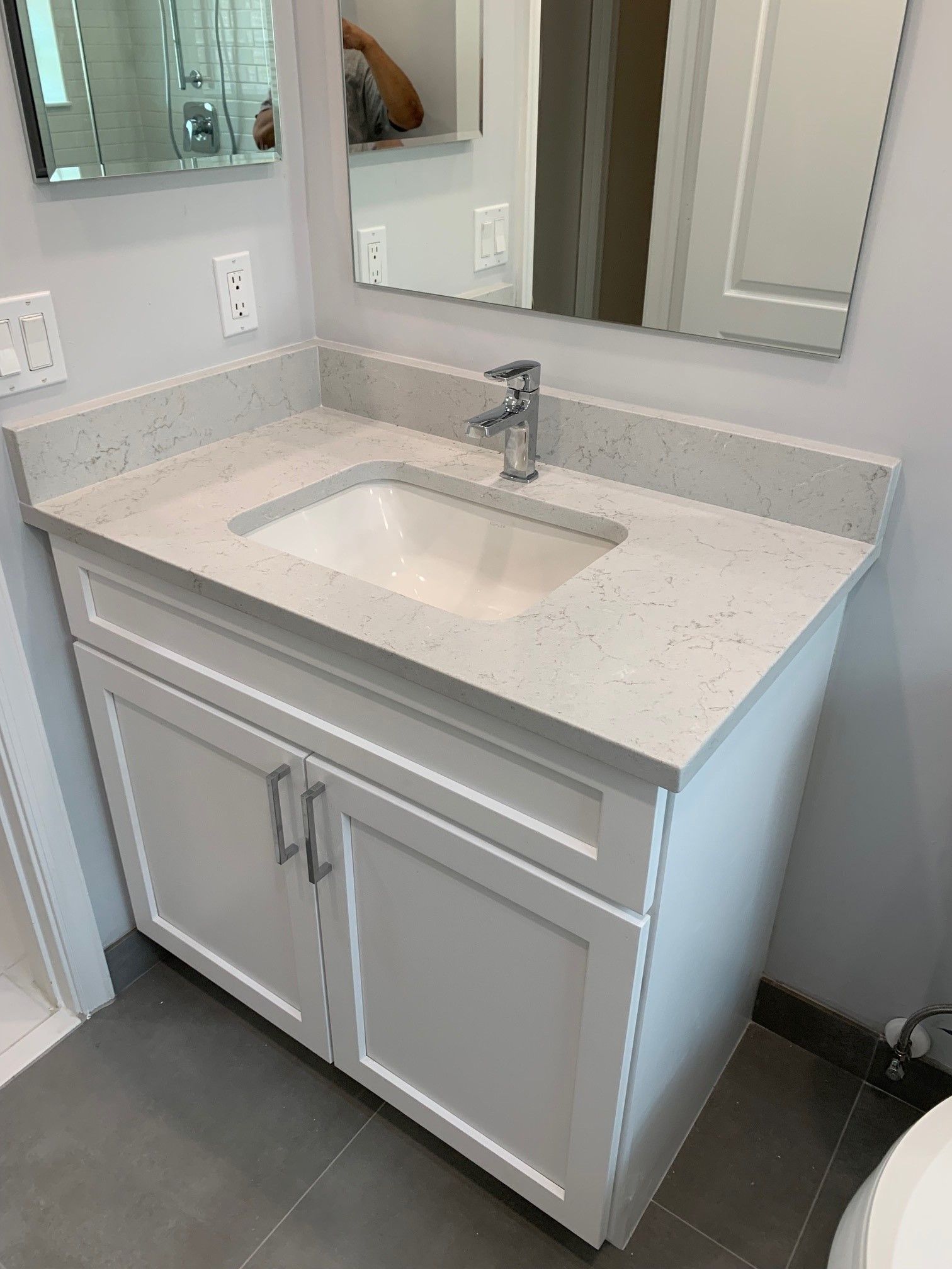 White bathroom vanity with a light gray countertop, rectangular sink, and two doors.