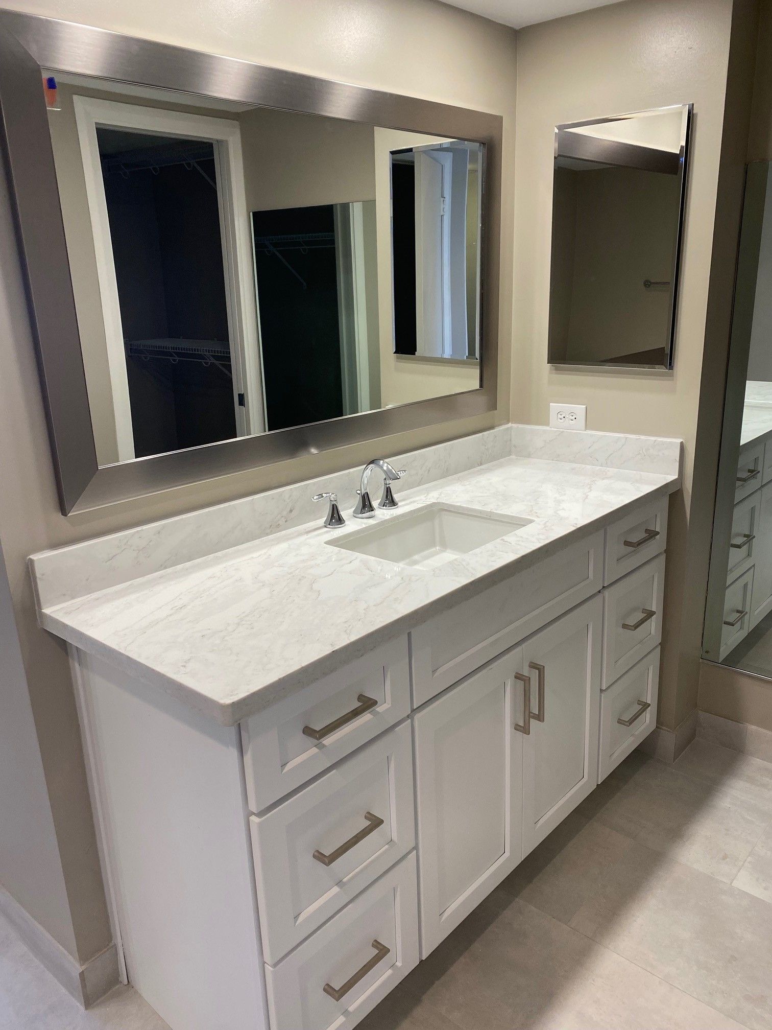 White bathroom vanity with marble countertop and large mirror.