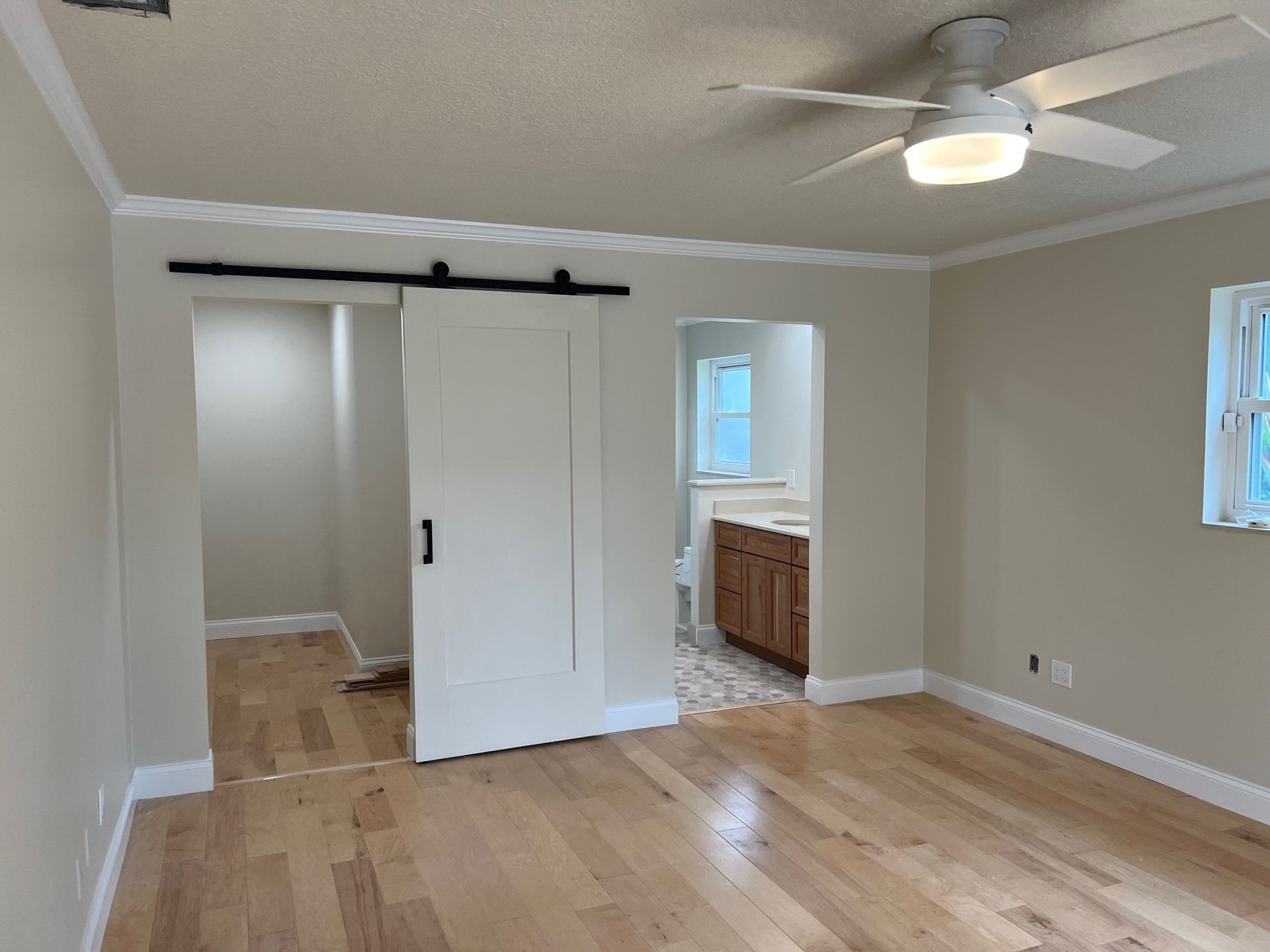 Bedroom with light wood floor, white walls and trim, sliding barn door, and a view of a bathroom.