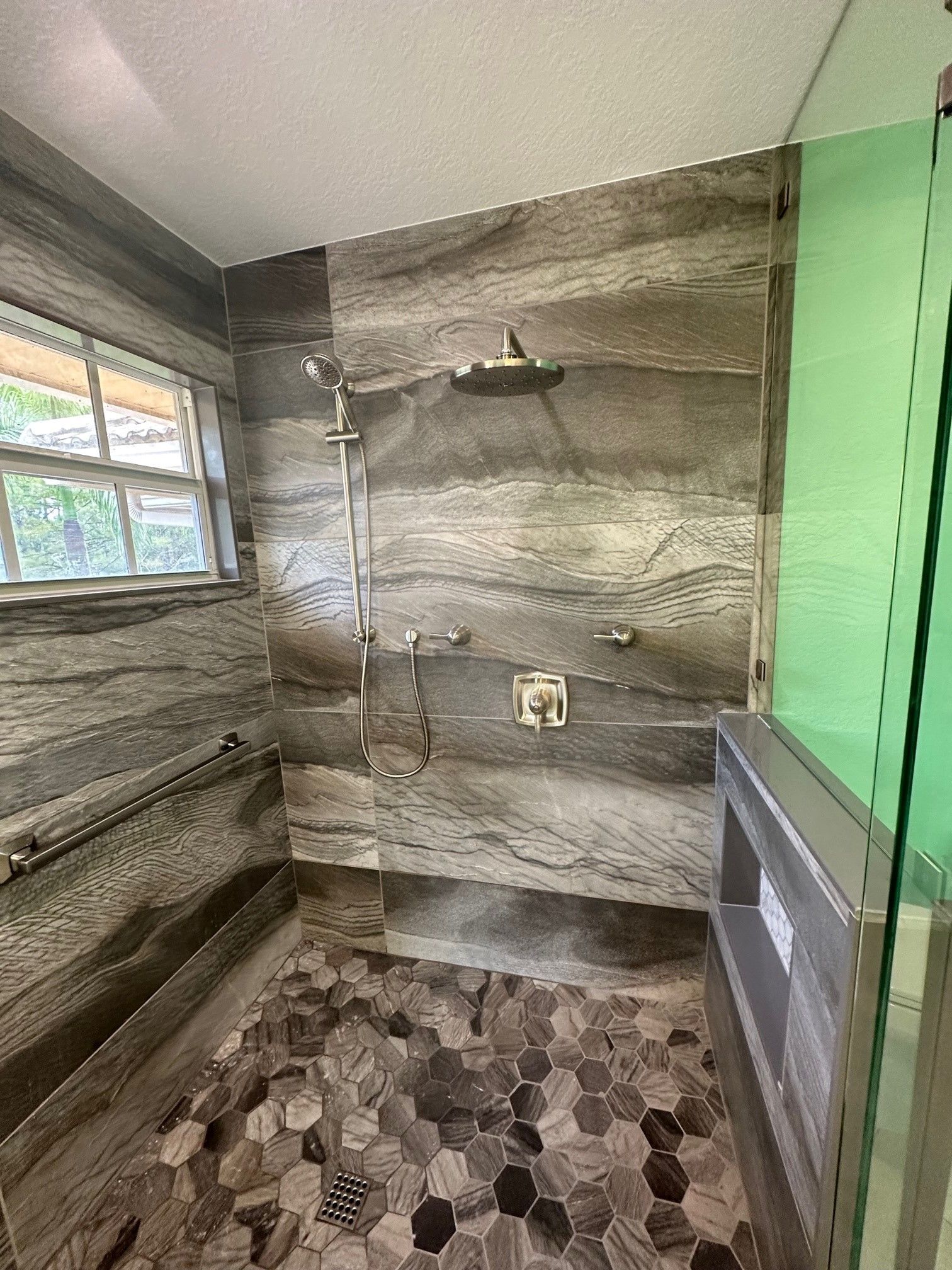 Bathroom with gray and brown stone tile shower, pebble floor, and glass enclosure.