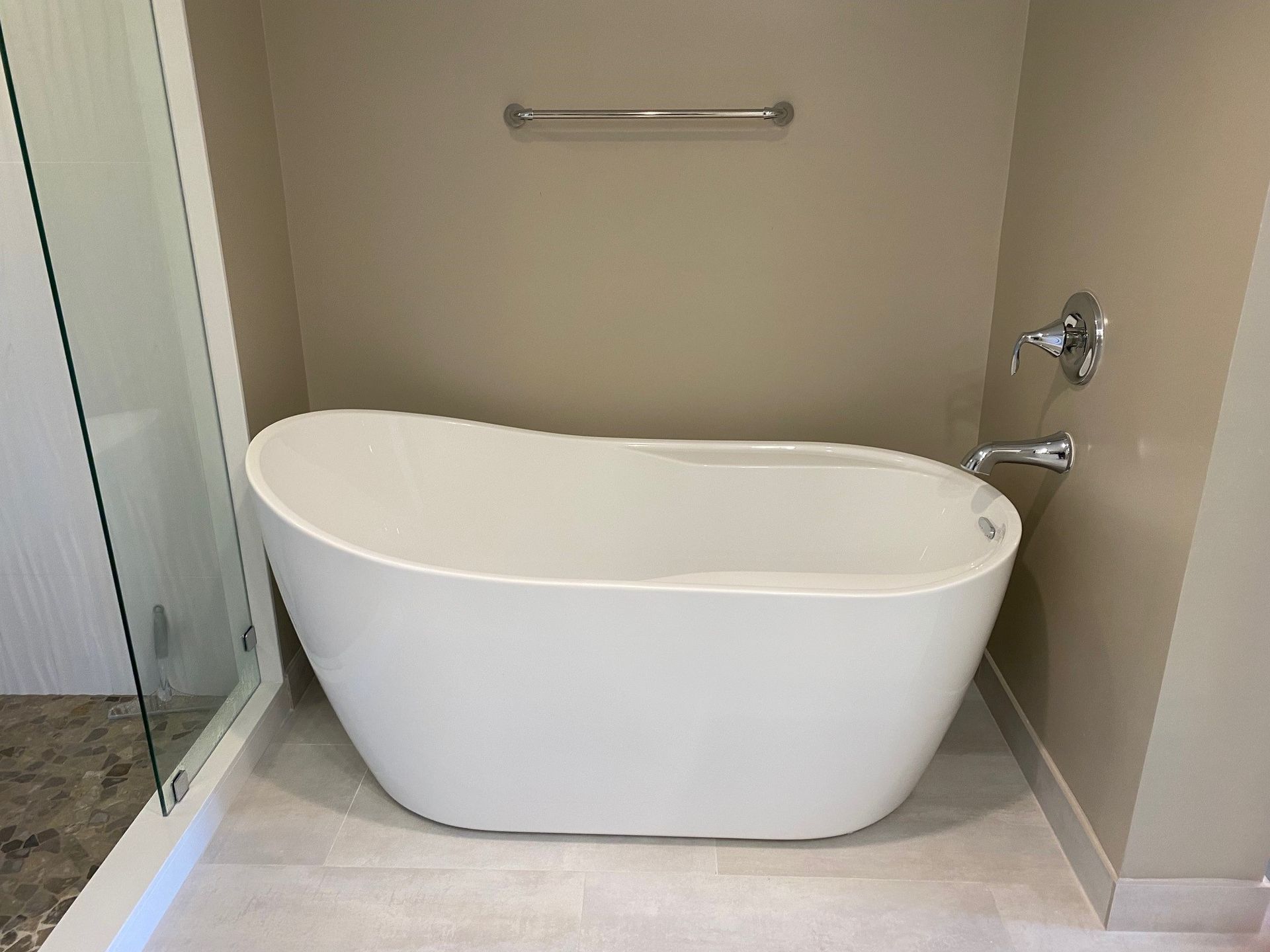 Freestanding white bathtub in a bathroom with beige walls and a chrome towel rack.
