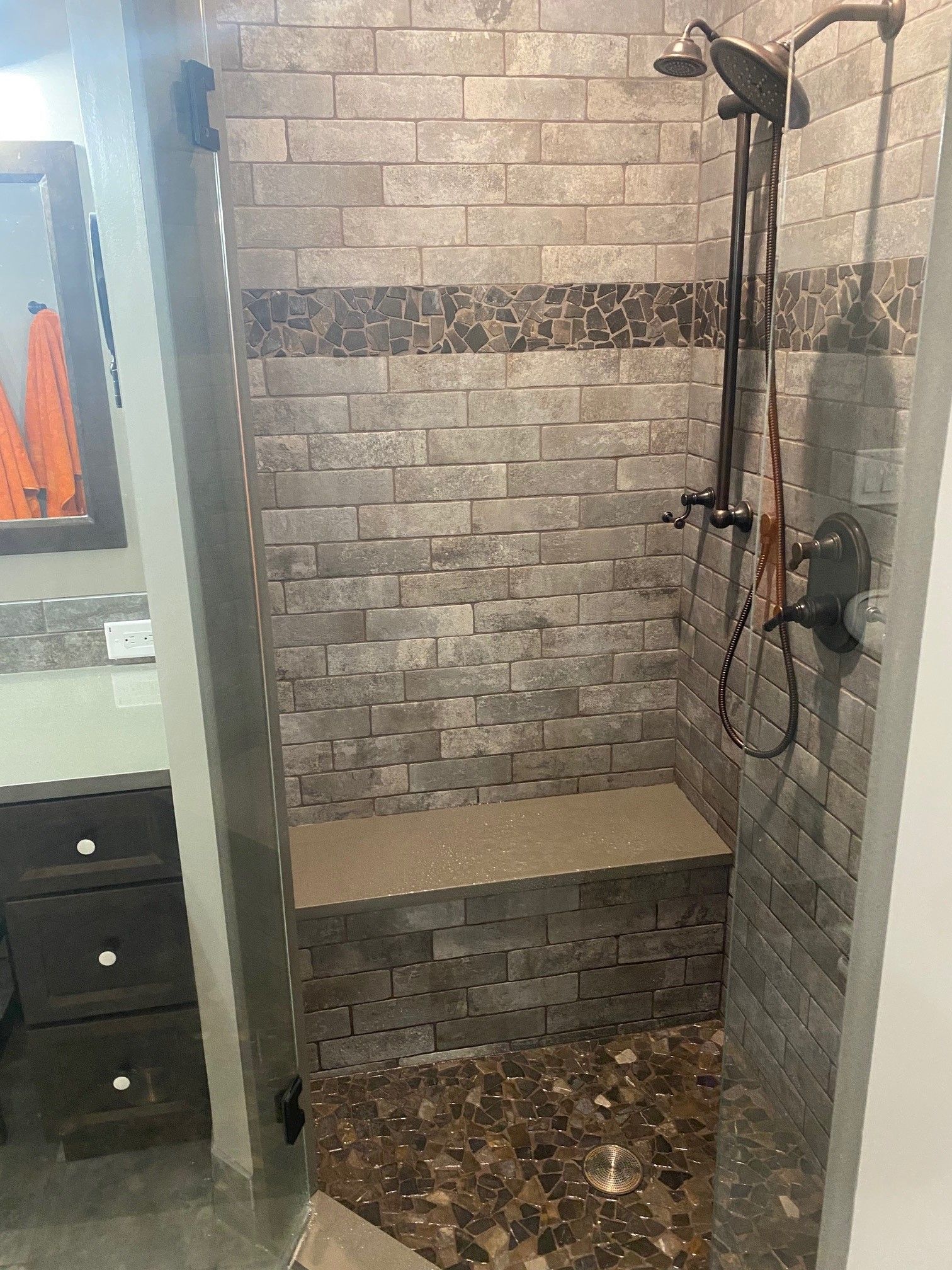 Tiled shower with a built-in bench, dark bronze fixtures, and a pebble floor.