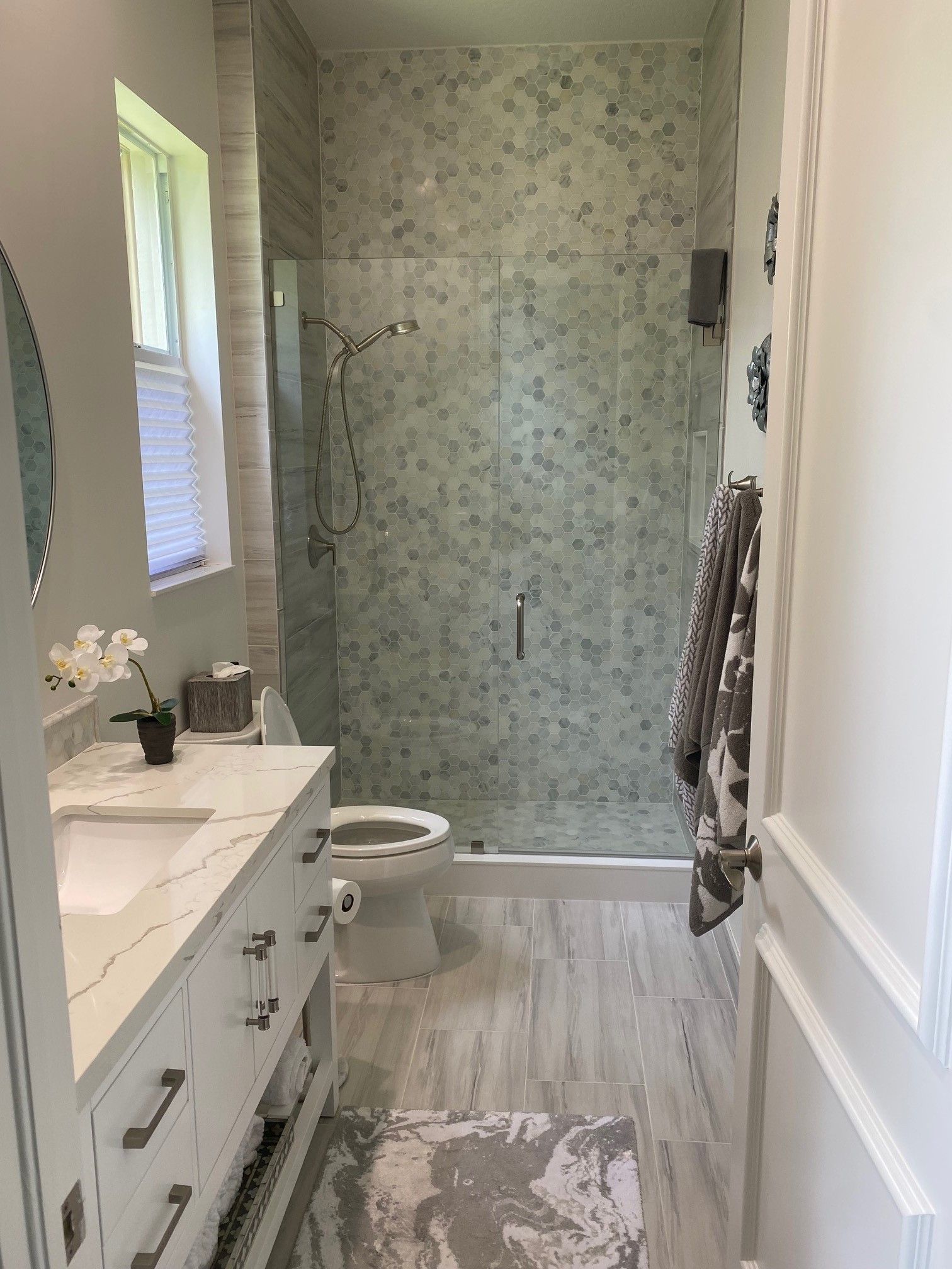 Bathroom with white vanity, patterned shower tile, and a glass door.