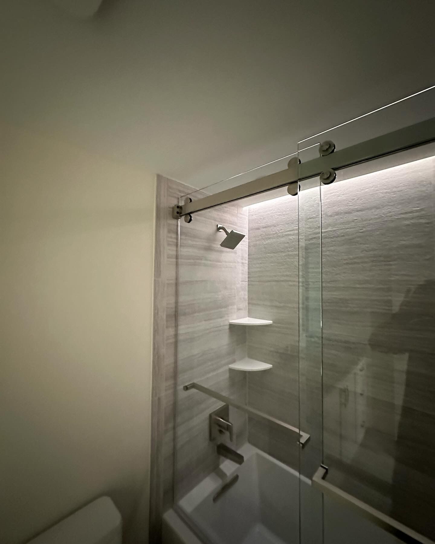 Modern bathroom with shower, glass door, and white tile.