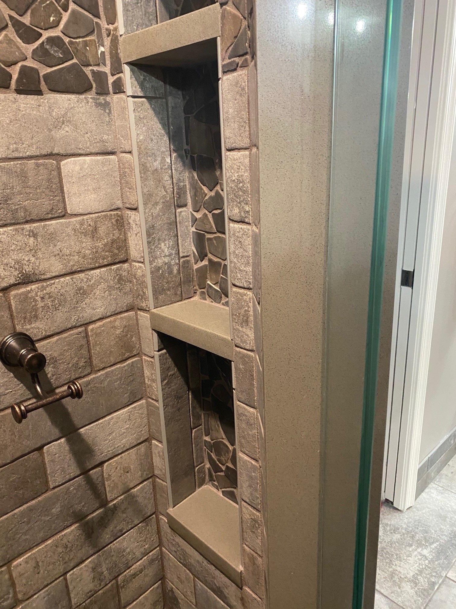 Shower with built-in shelves: stone tile and a glass door. Neutral colors: gray and brown.