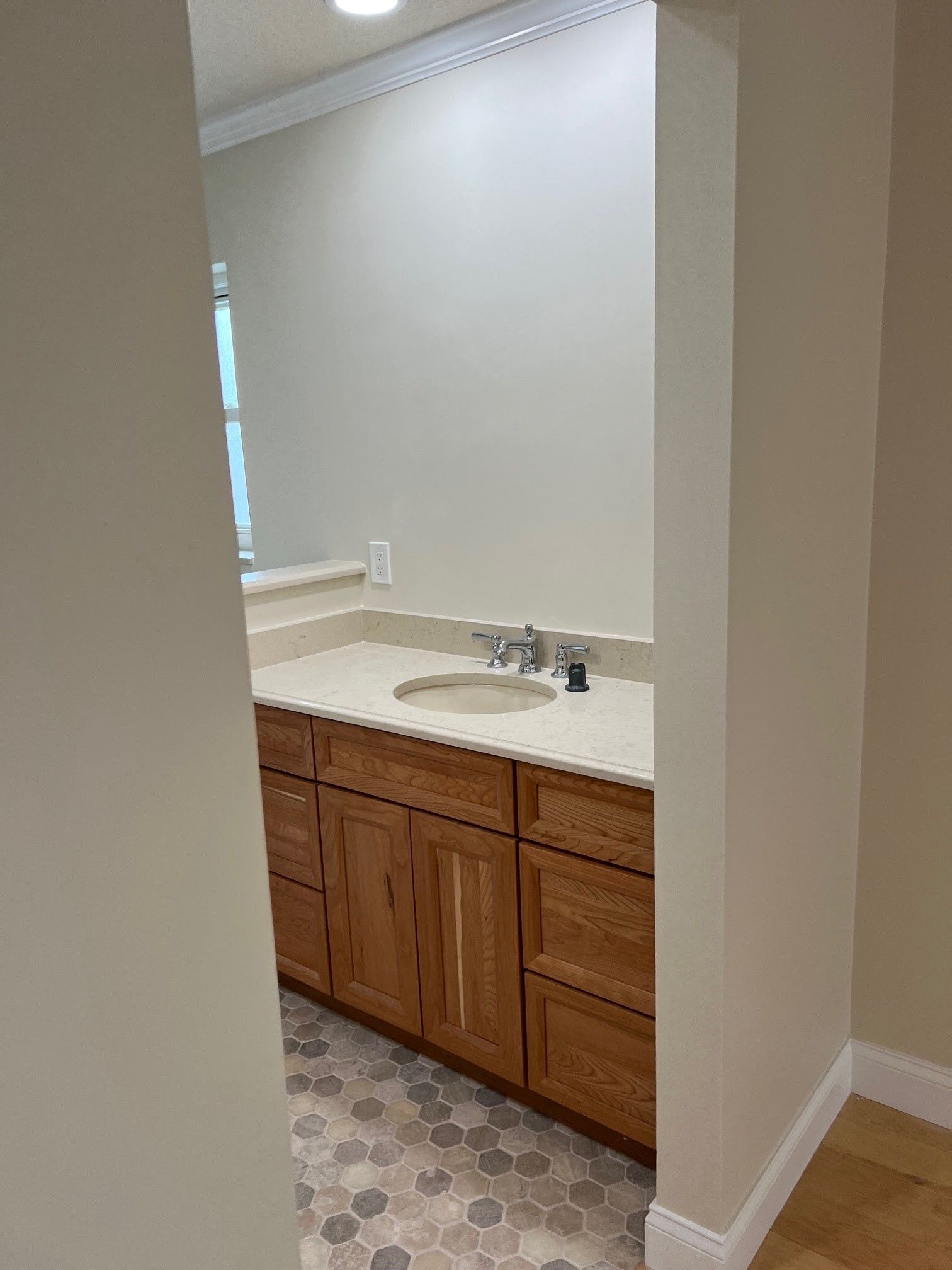 Bathroom with light-colored walls, wood cabinets, and a sink. Hexagonal floor tiles.