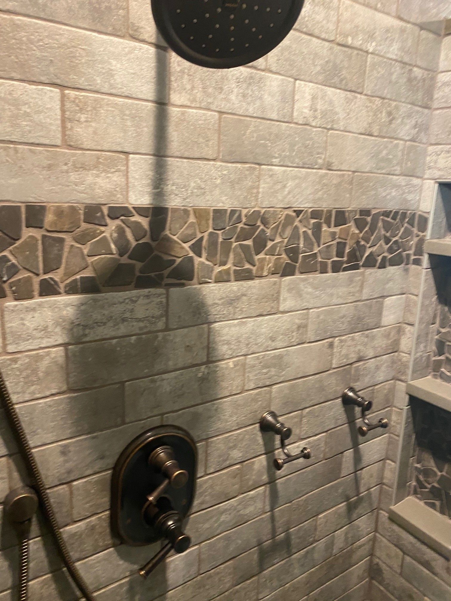 Shower with gray rectangular tiles, a stone accent, and bronze fixtures.