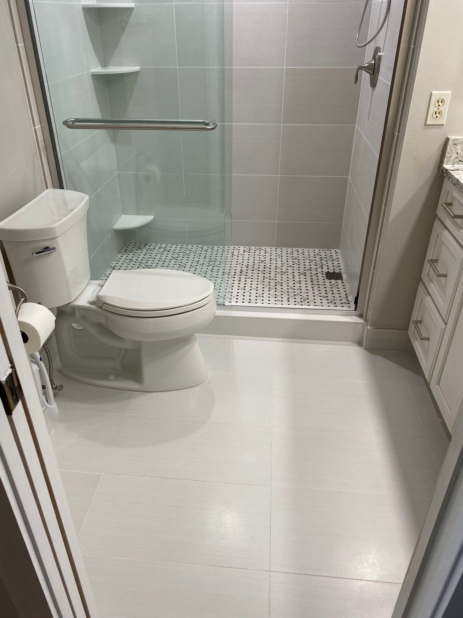 White bathroom with glass shower, toilet, and vanity. Gray walls and white floor.