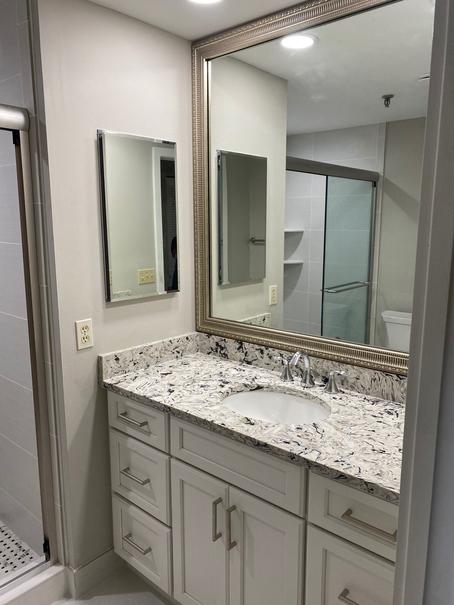 Bathroom vanity with white cabinets, granite countertop, two mirrors, and a glass shower door.