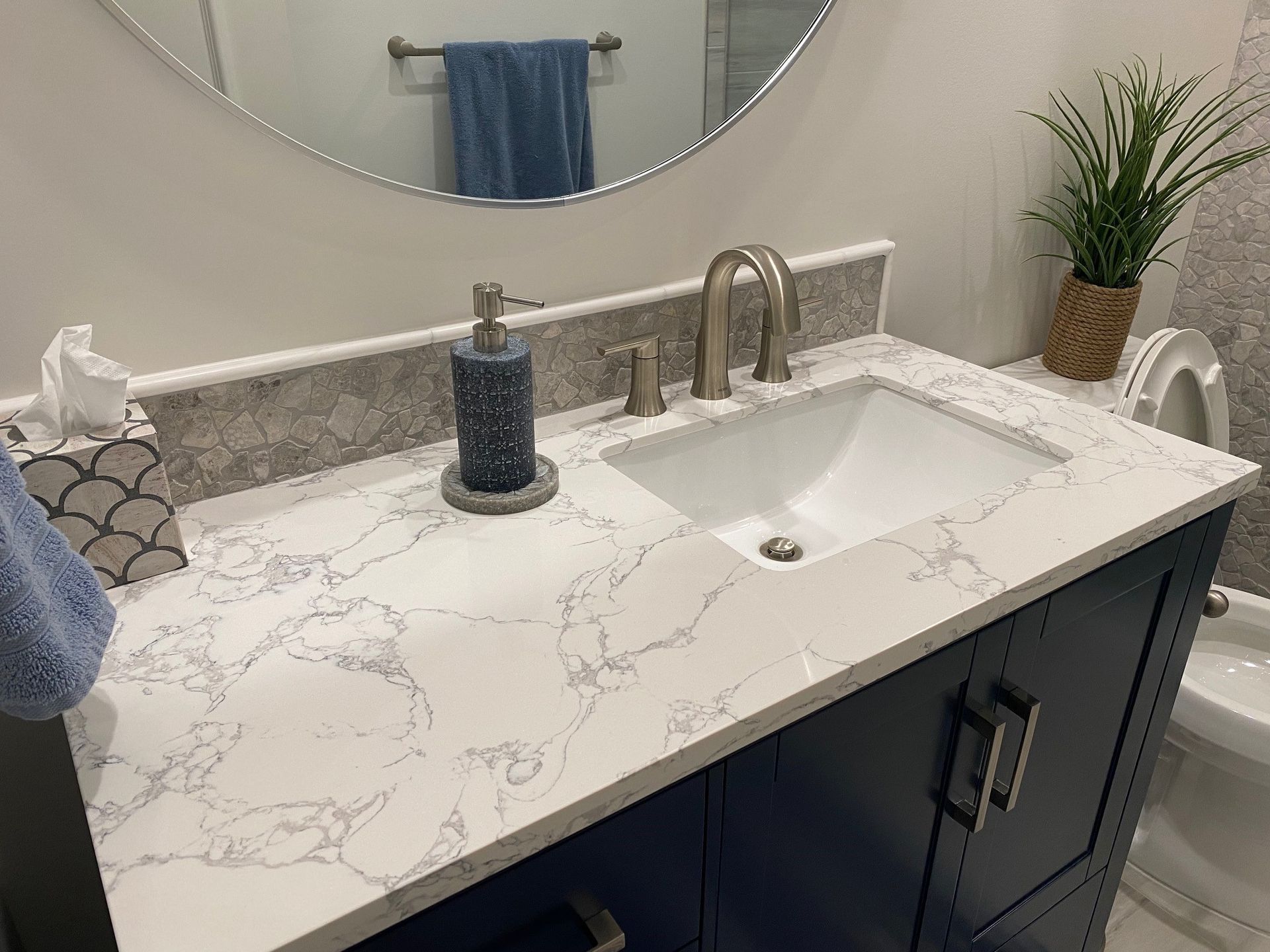 Bathroom vanity with quartz countertop and dark blue cabinet. White sink and gray backsplash.