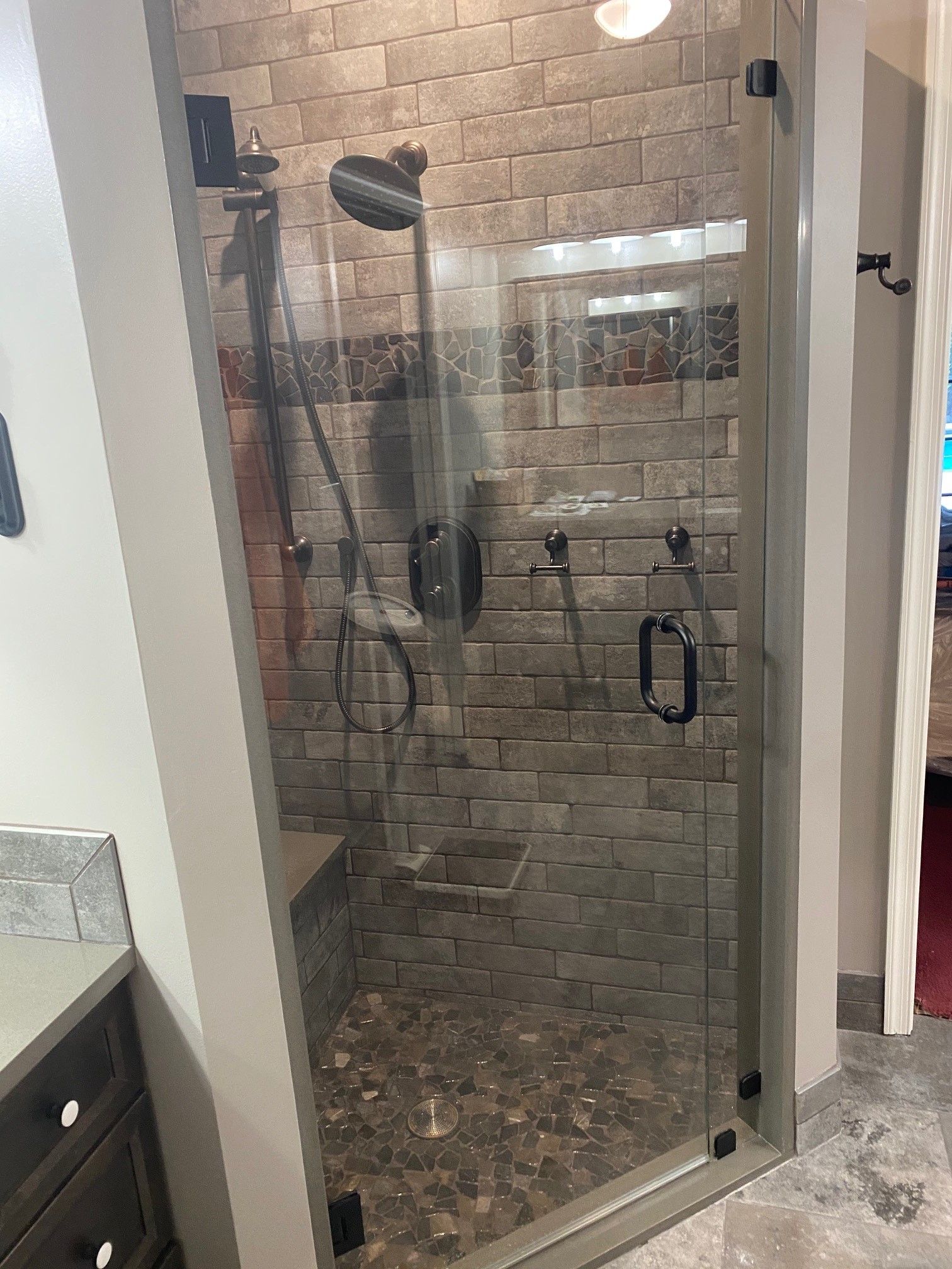Glass shower enclosure with pebbled floor and stone tile walls.