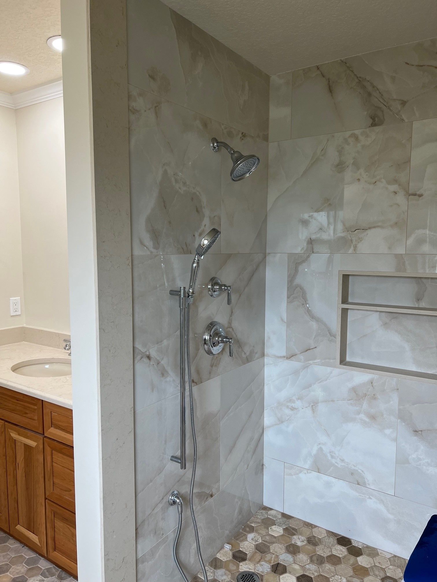 Shower with marble-look tile and multiple shower heads, with a built-in shelf.