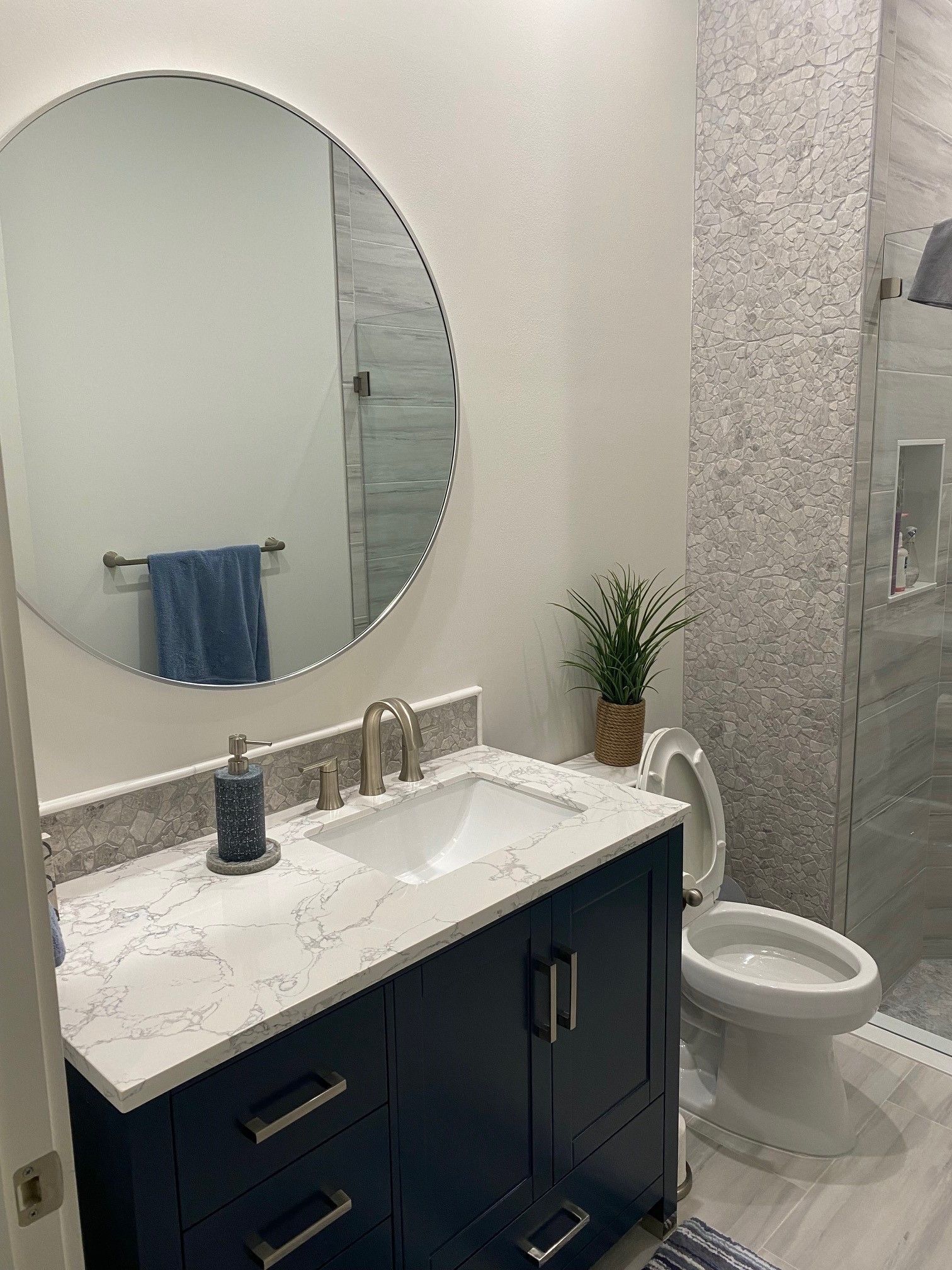 Bathroom with navy vanity, white countertop, round mirror, and tiled shower.