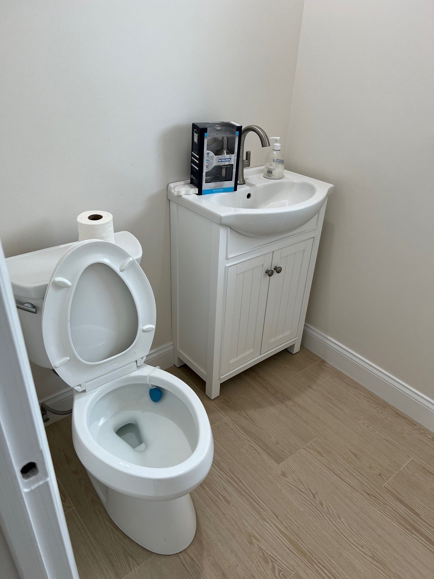 White toilet with open seat, beside a white sink cabinet in a small bathroom.