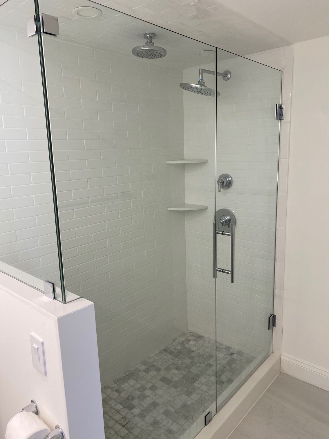 Glass-walled shower with white subway tile, two shower heads, and marble floor.