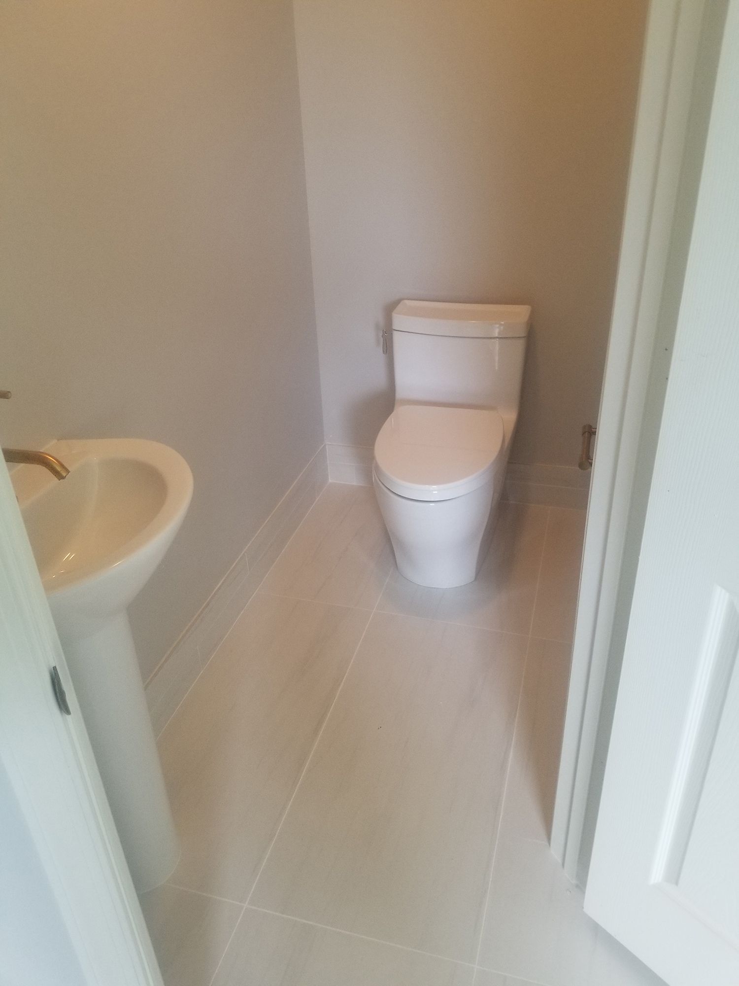 Small bathroom with a white toilet and pedestal sink, light tile floor.