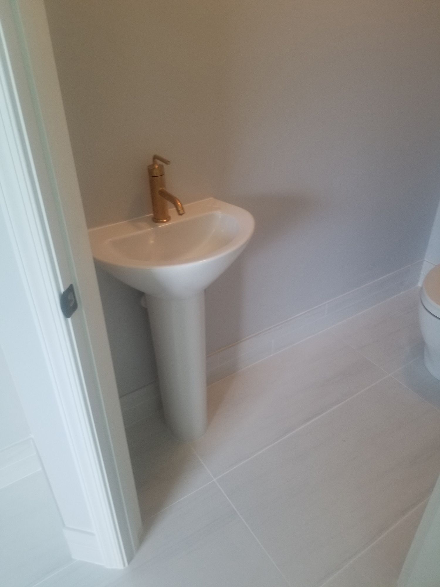 White pedestal sink with gold faucet in a small bathroom.