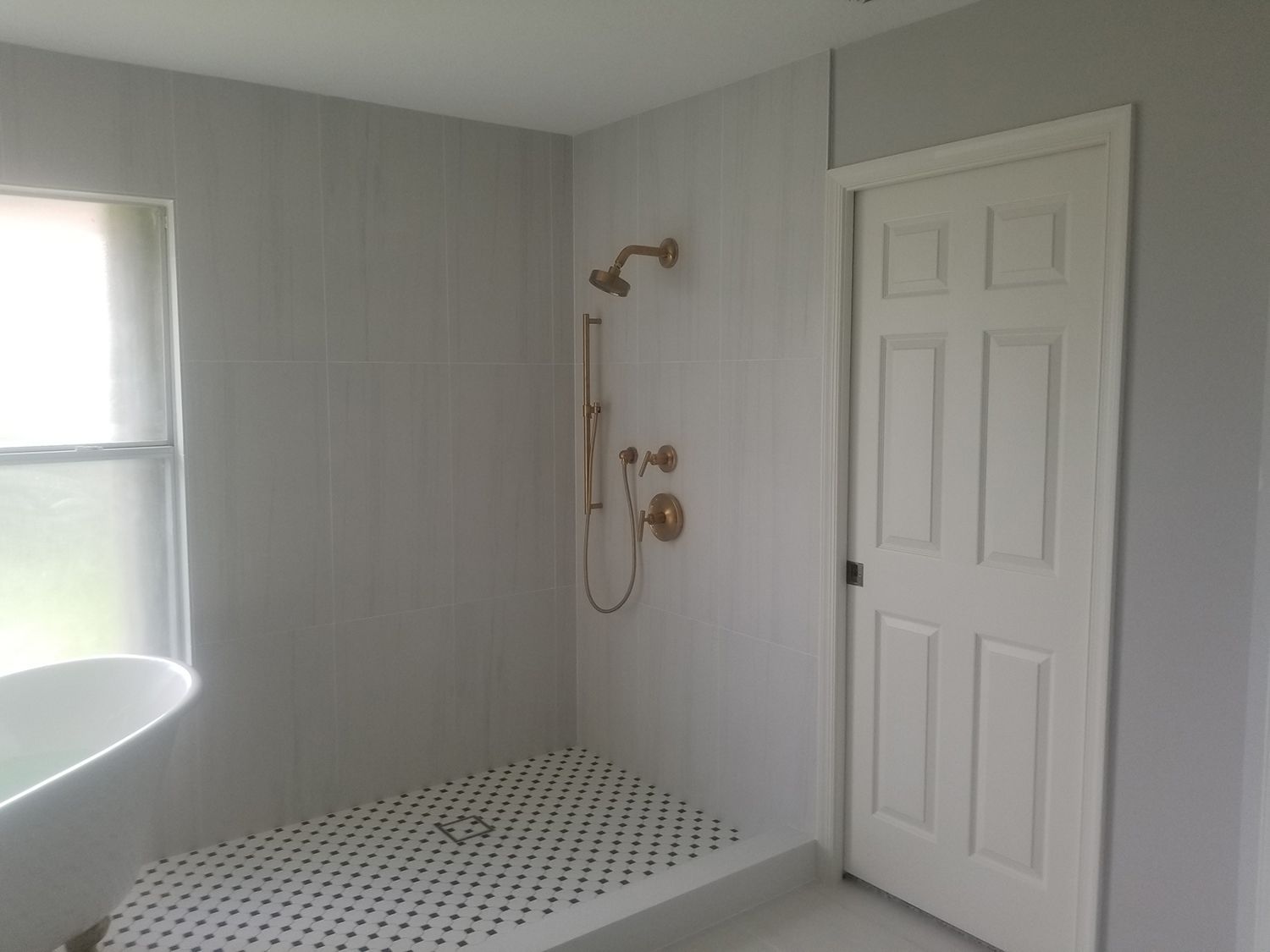 Bathroom remodel with a white door, brass shower fixtures, and black and white tiled shower floor.