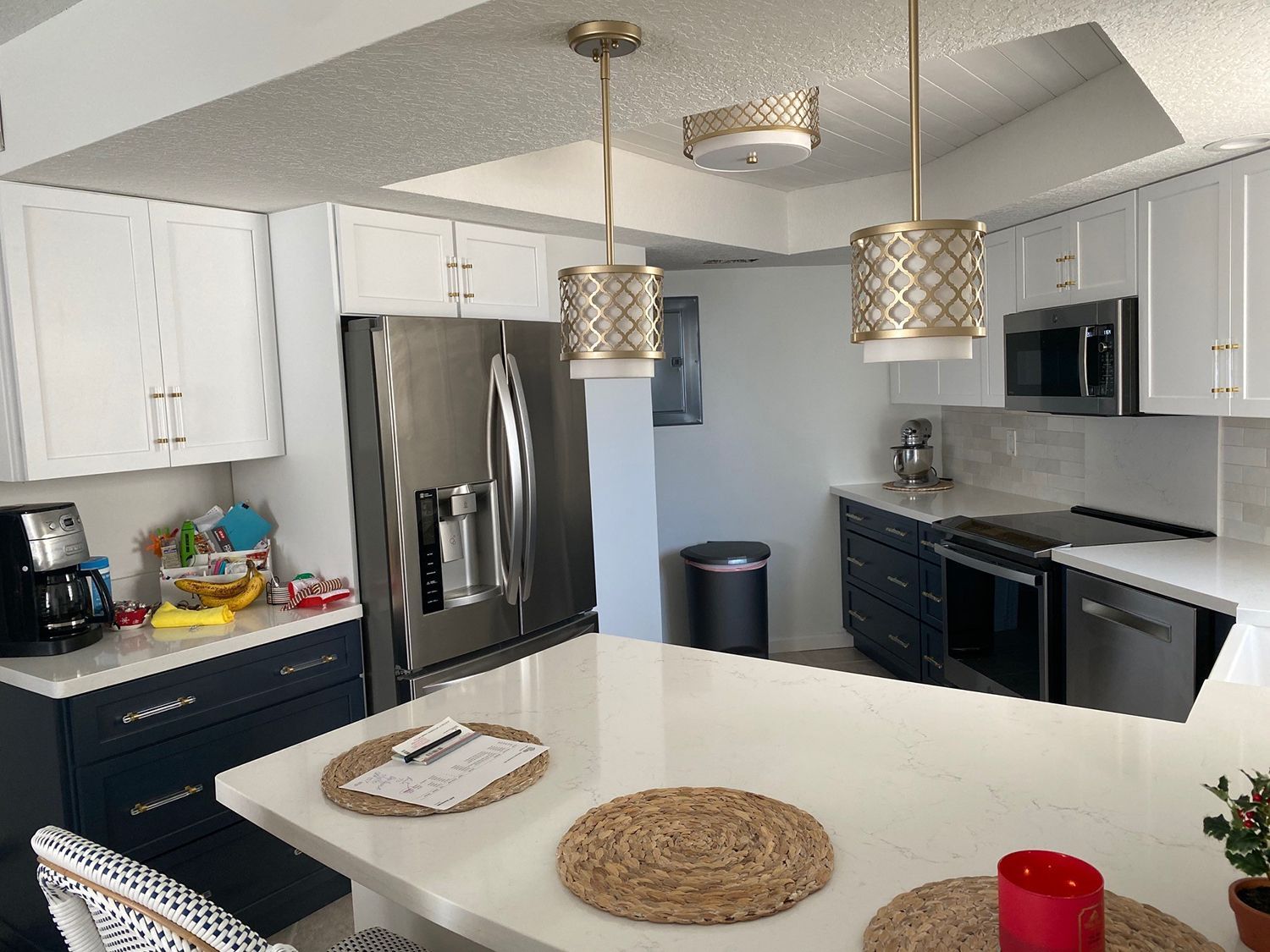 Modern kitchen with white and dark blue cabinets, stainless steel appliances, and pendant lights.
