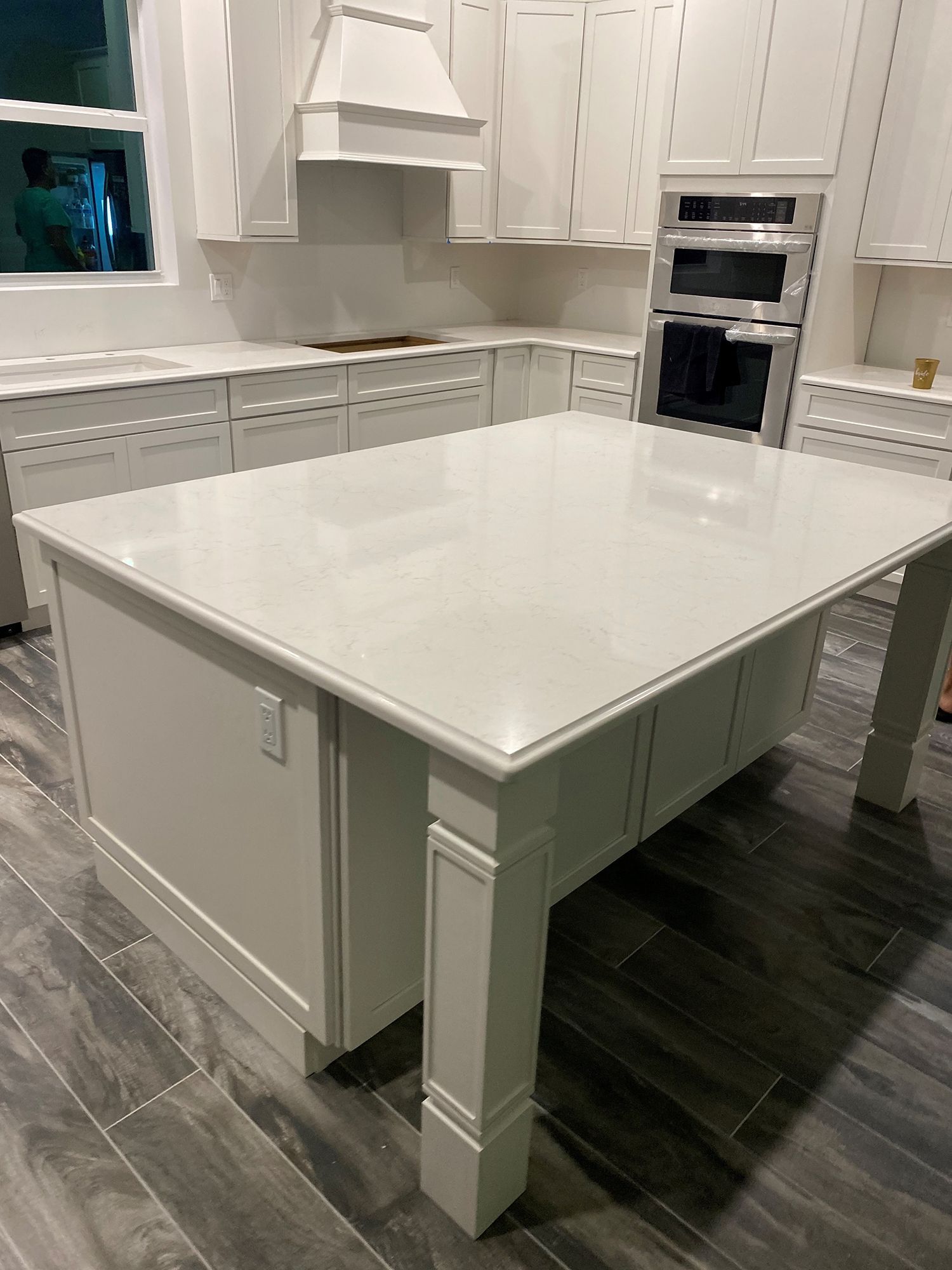 White kitchen with island, cabinets, range hood, and double oven. Light grey tile floor.