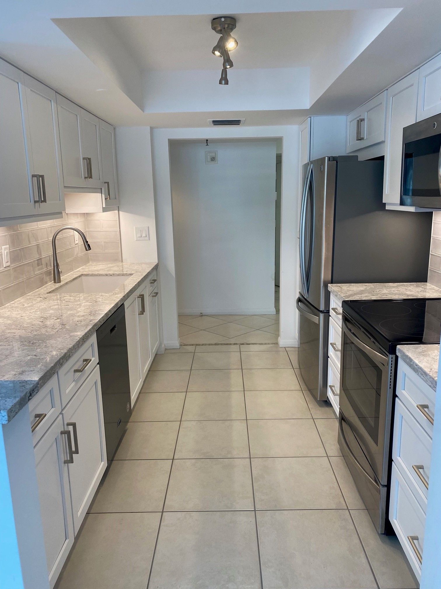 Narrow kitchen with white cabinets, stainless steel appliances, and gray countertops.
