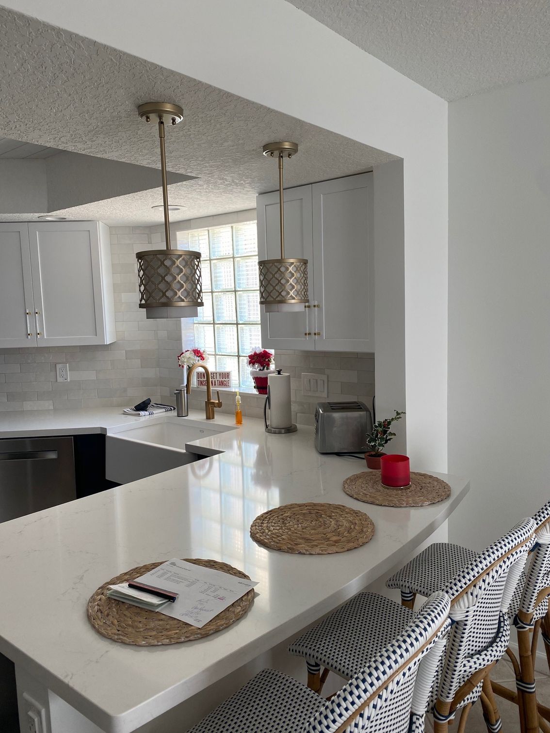 Kitchen with white cabinets, countertop, two pendant lights, and bar stools.