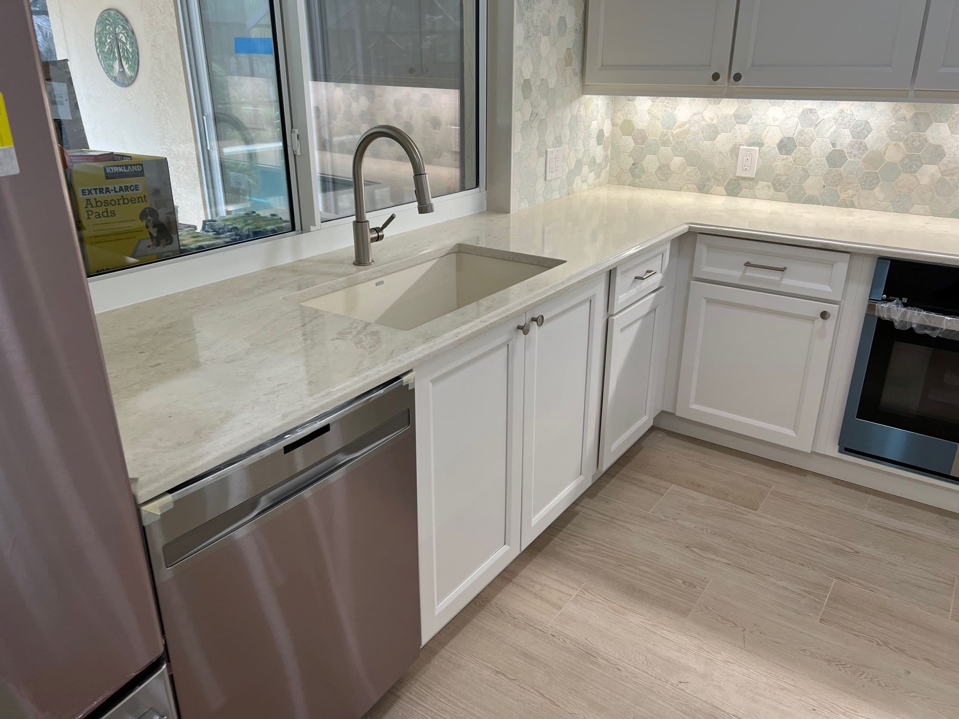 Kitchen with white cabinets, stainless steel dishwasher, and a sink beneath a window.