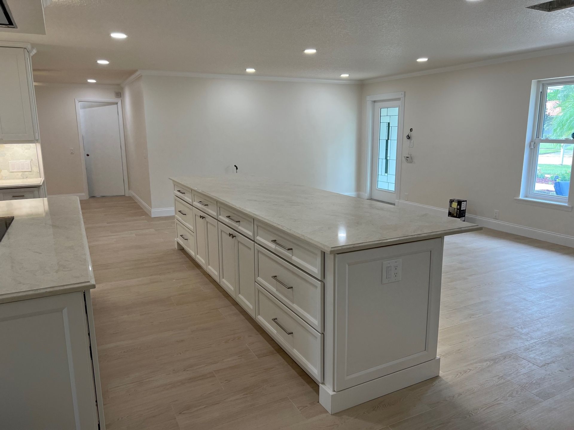 Newly renovated kitchen with a white island and countertops, light wooden floors, and white walls.