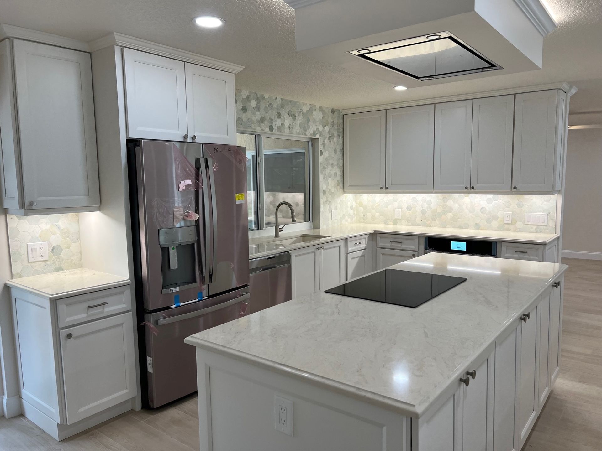 White kitchen with island, stainless steel refrigerator, and light countertops.