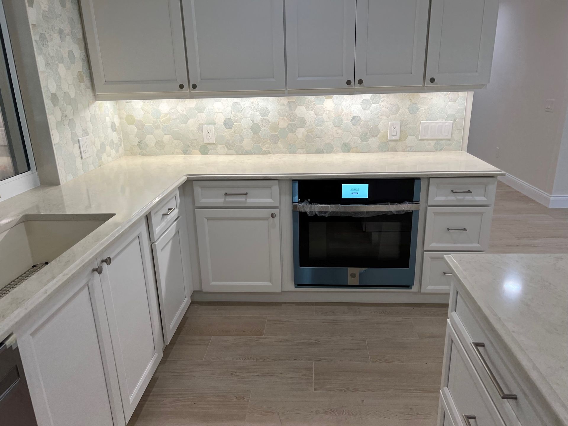 White kitchen with light countertops, hexagon backsplash, built-in oven, and cabinets.