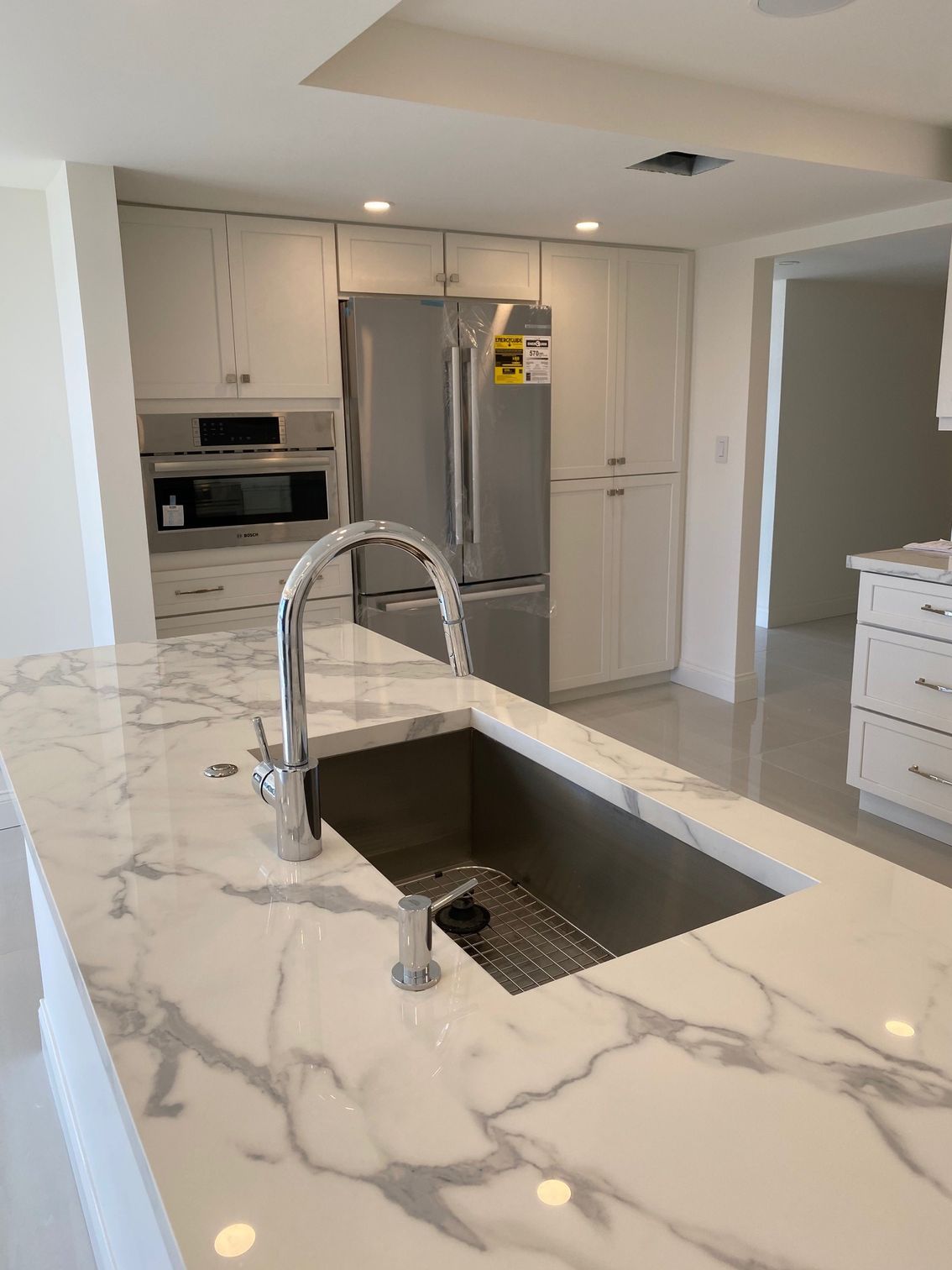 Modern kitchen with marble countertop, stainless steel sink, and light gray cabinets.