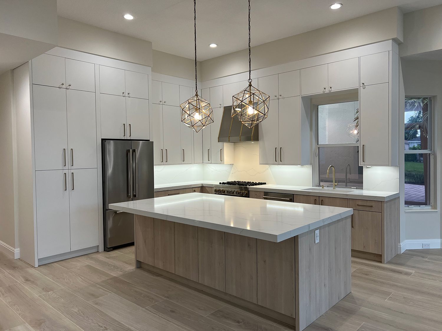 Modern kitchen with white cabinets, island, stainless steel appliances, and pendant lights.