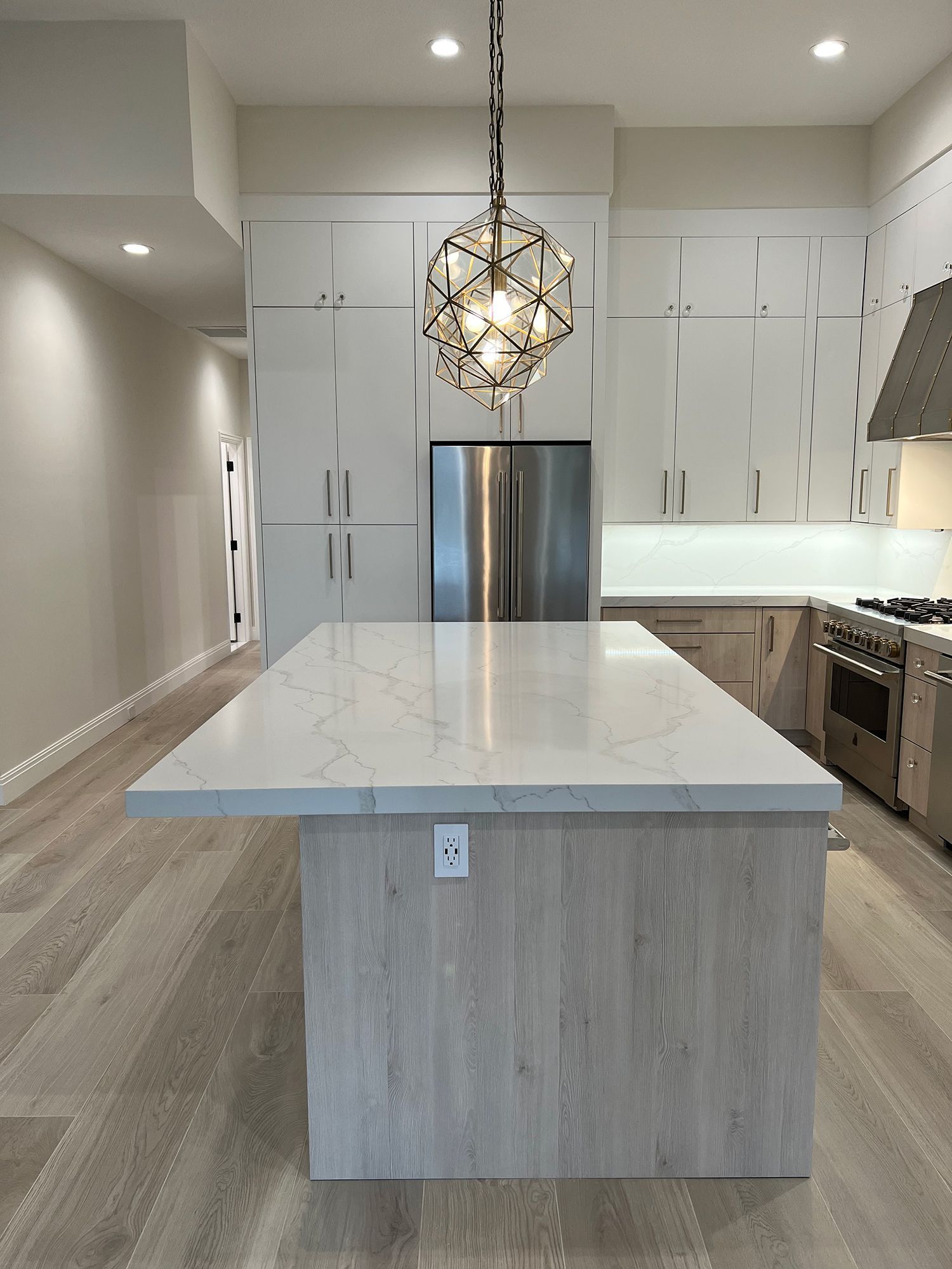 Modern kitchen with light wood floor and cabinets, stainless steel appliances, and large island with stone countertop.