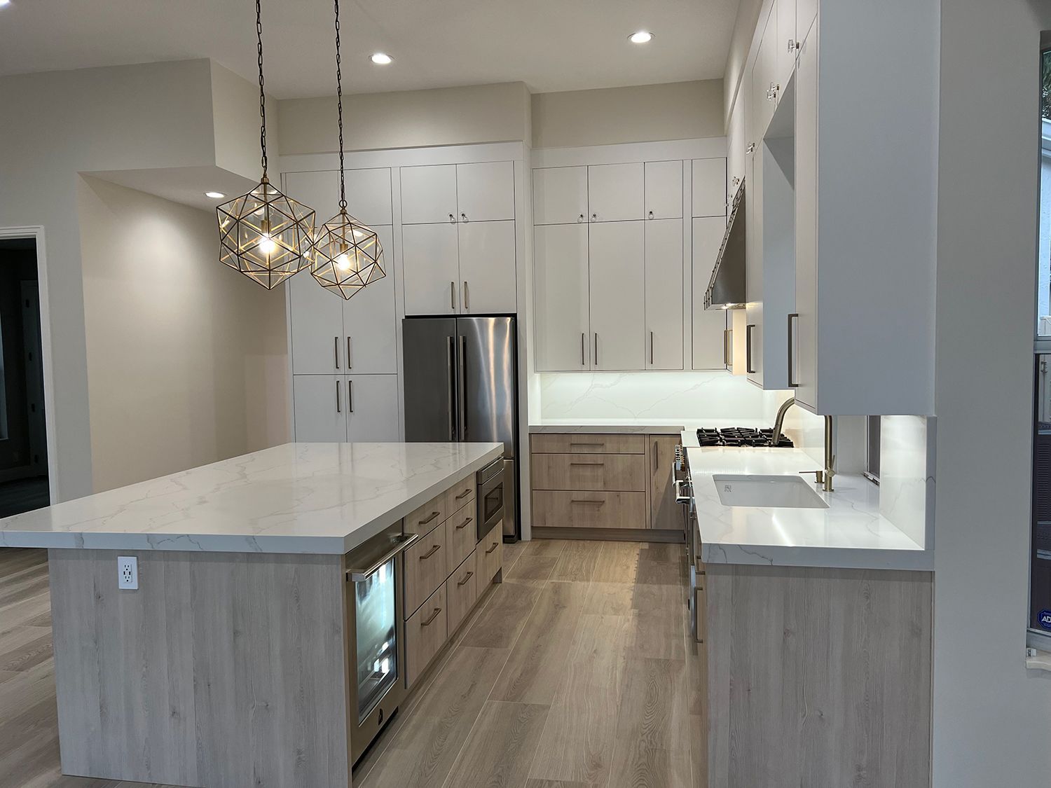 Modern kitchen with light wood cabinets, stainless steel appliances, and white countertops.