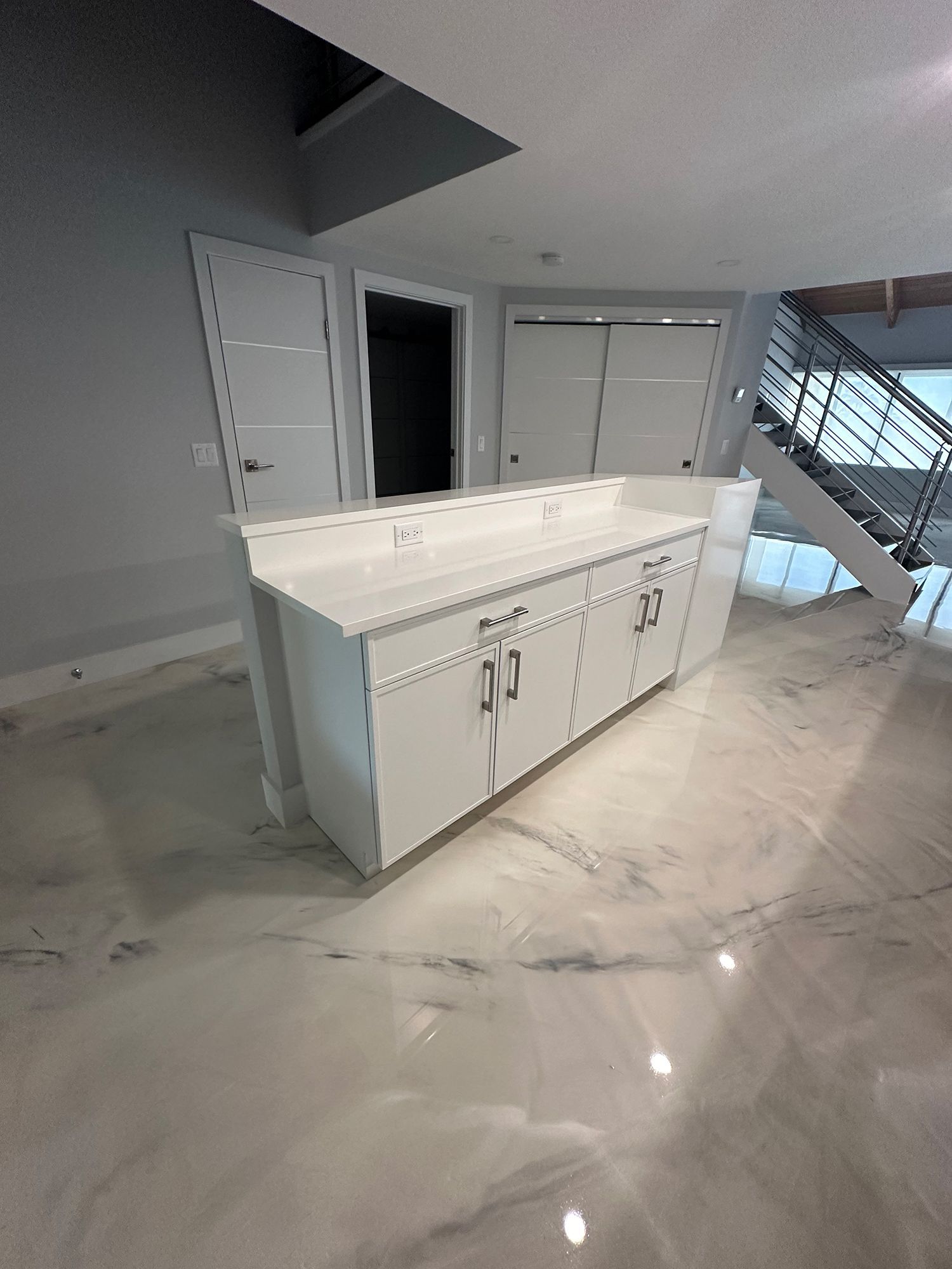 White kitchen island with countertop in a modern, light-filled space. Closets, doors, and stairs visible.