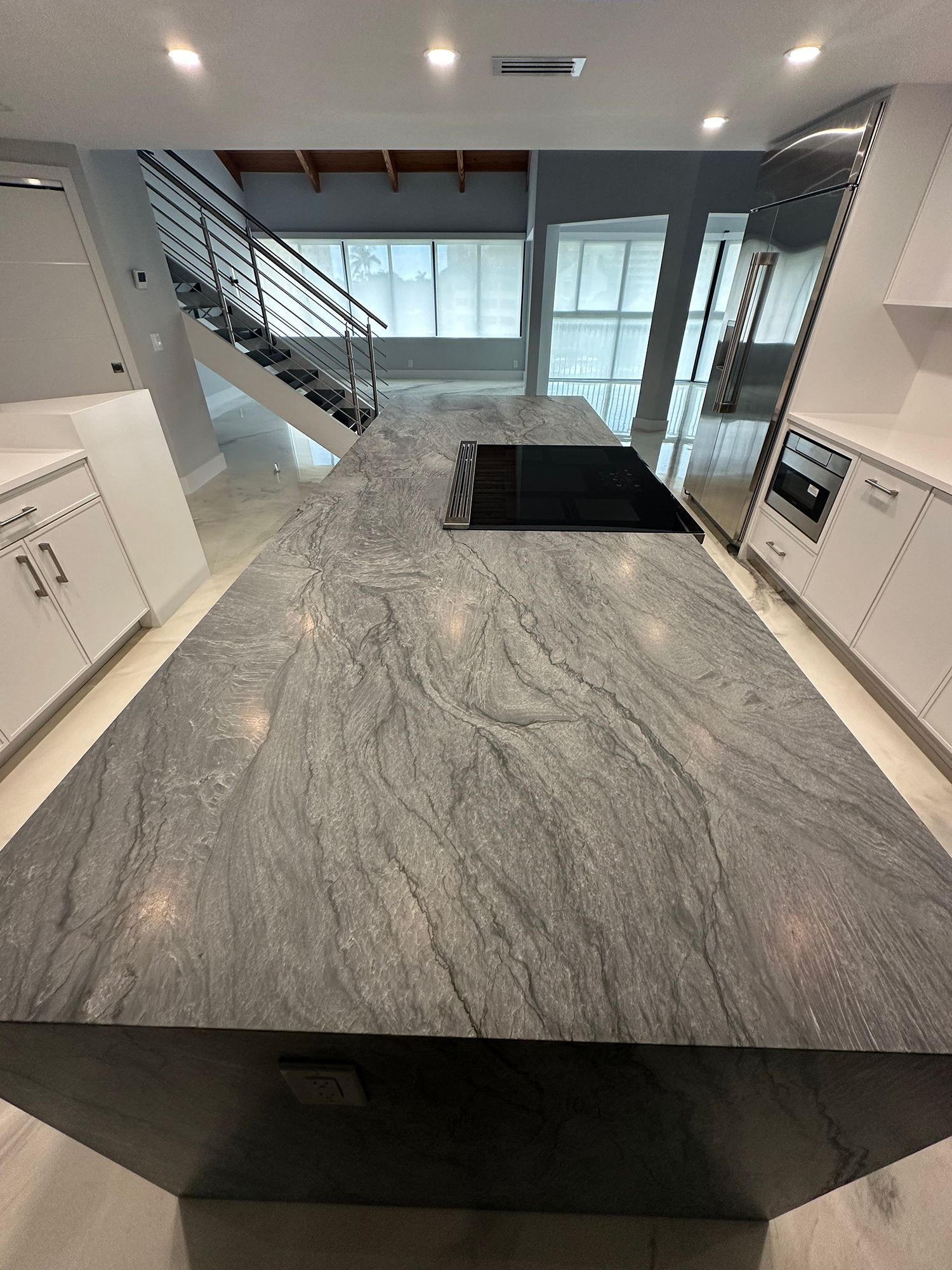 Gray granite countertop in a modern kitchen, with a built-in cooktop, overlooking the stairs.