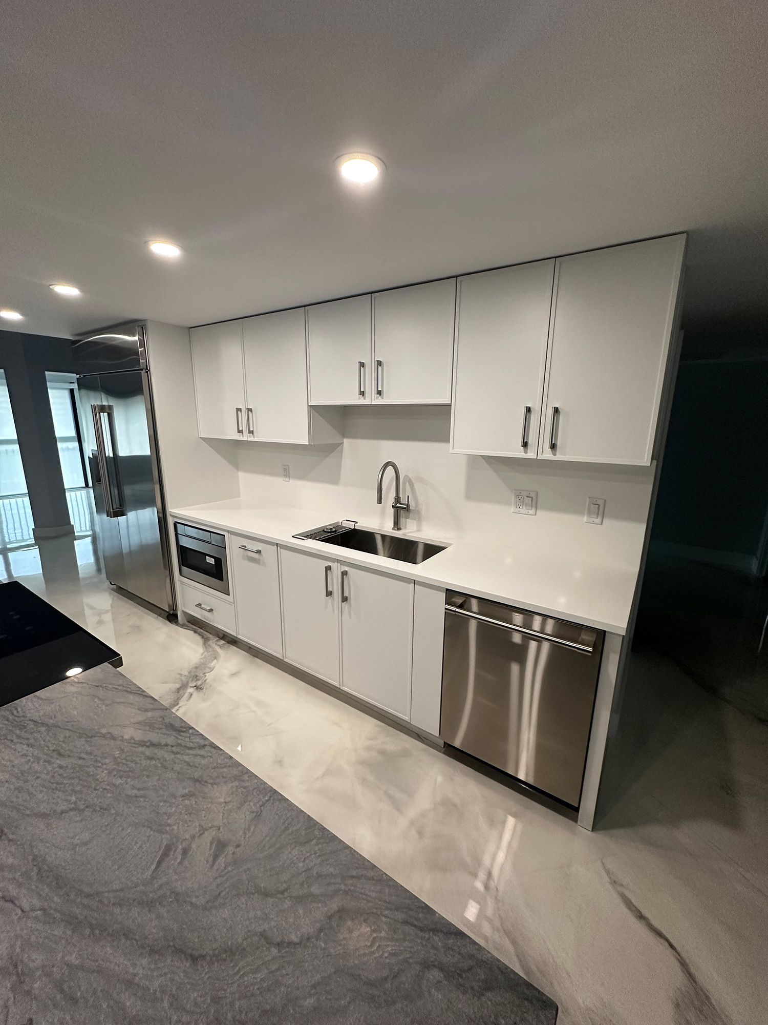 Modern white kitchen with stainless steel appliances, marble countertop, and white cabinets.