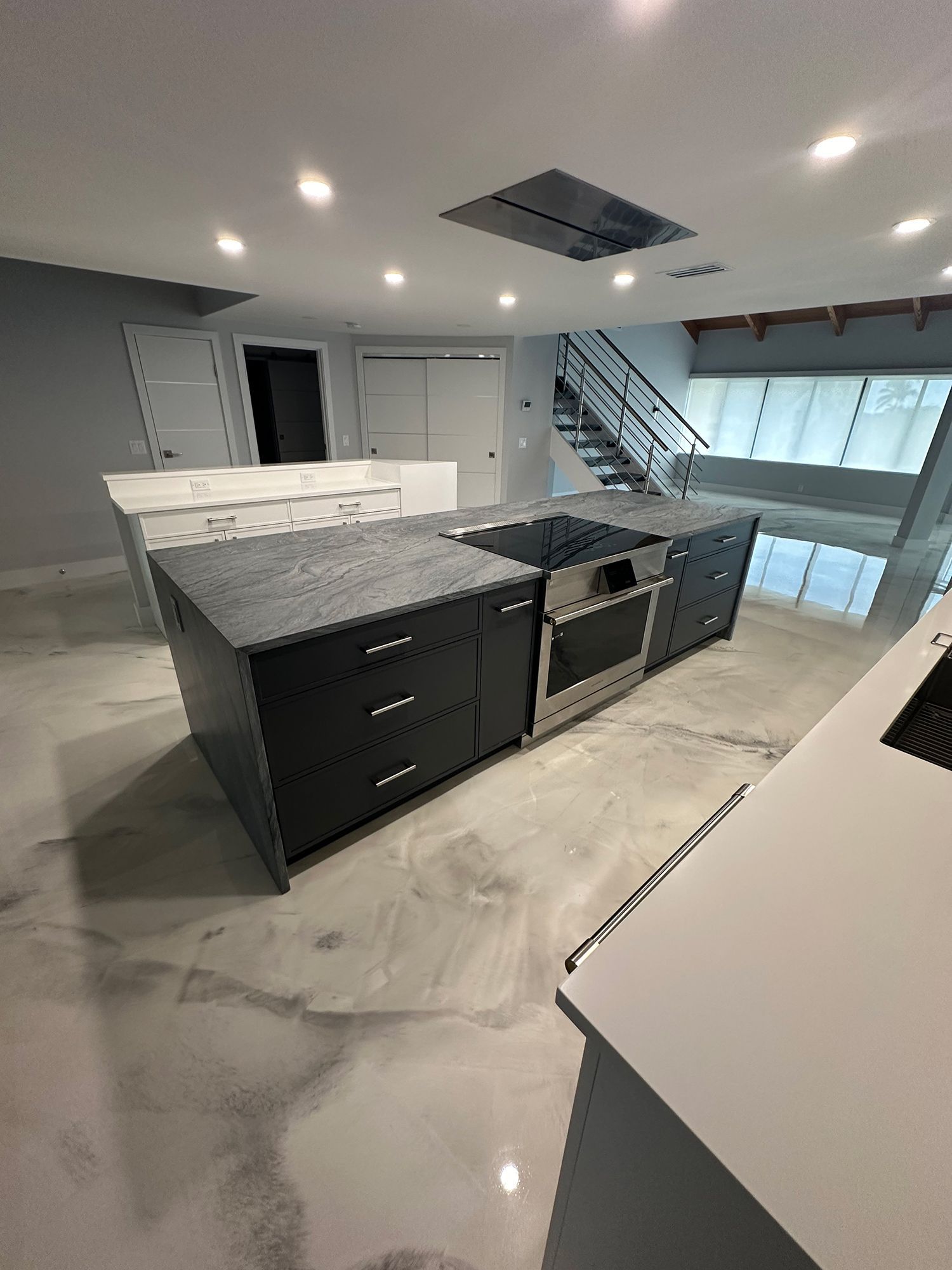 Modern kitchen with a black island, cooktop, and drawers. Light gray floor and cabinets, stainless steel appliances.