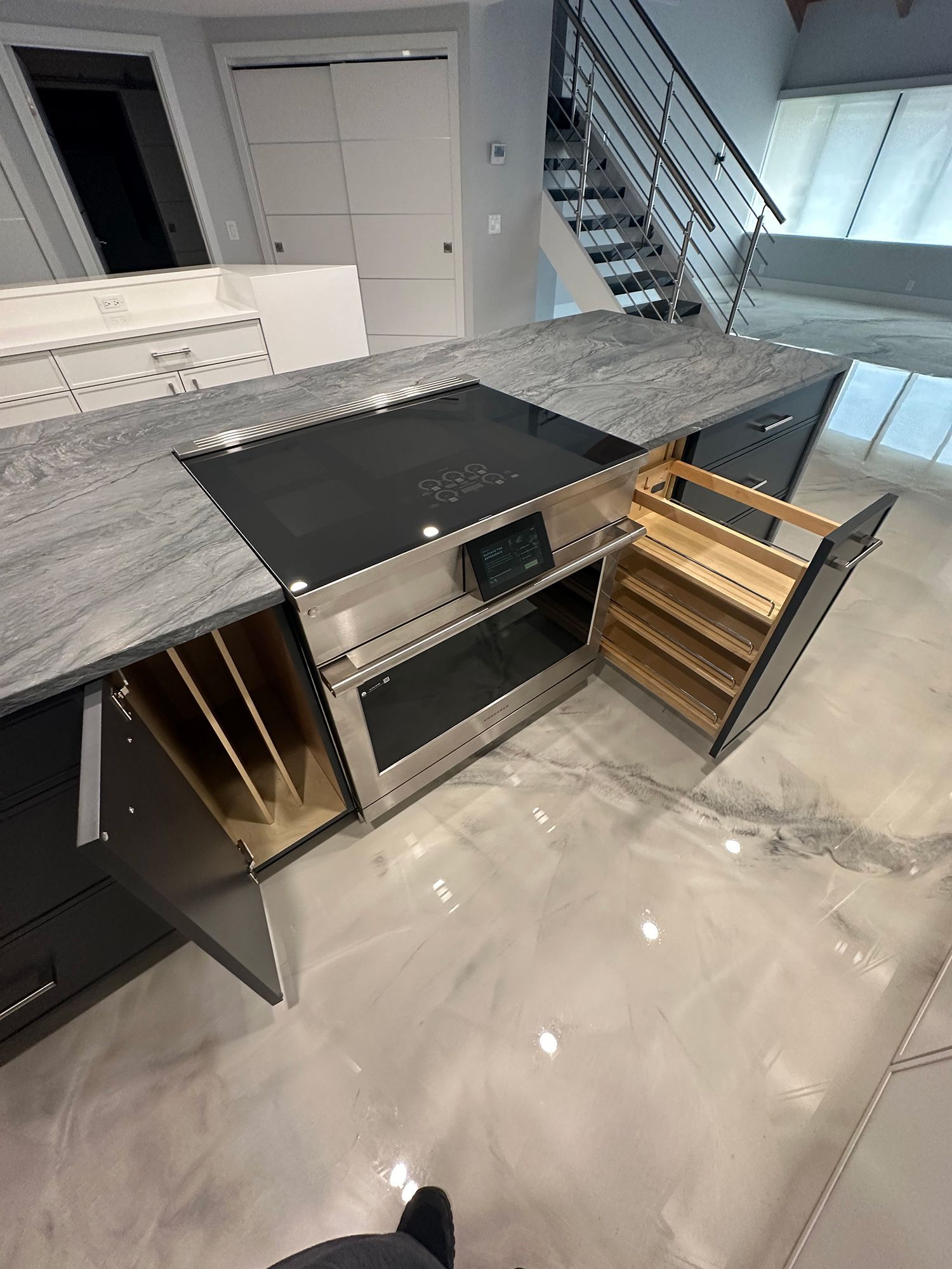 Modern kitchen island with stovetop, oven, and open storage drawers. Grey countertop and glossy floor.