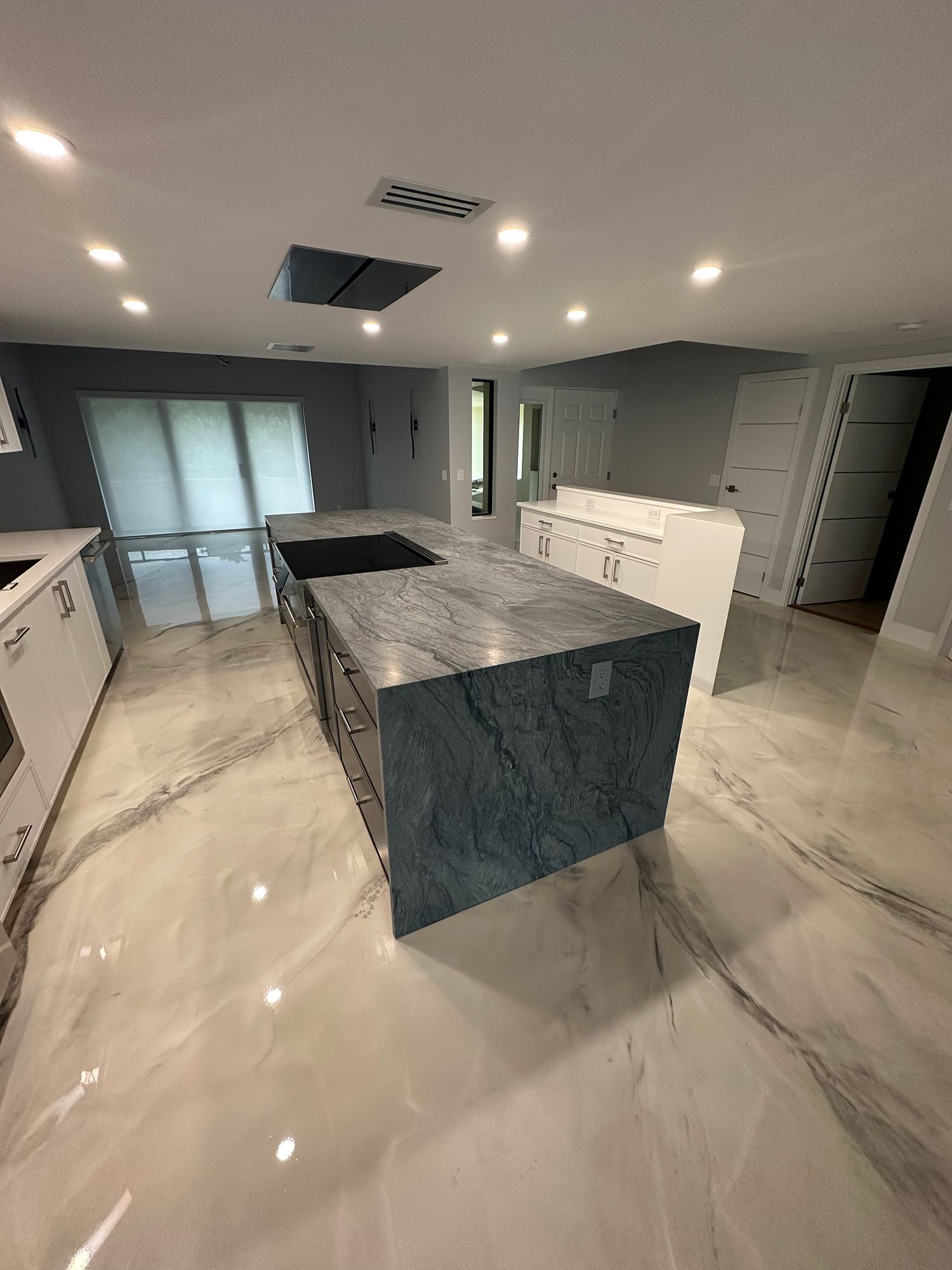 Newly renovated kitchen with a large island, gray countertops, and shiny, light-colored flooring.