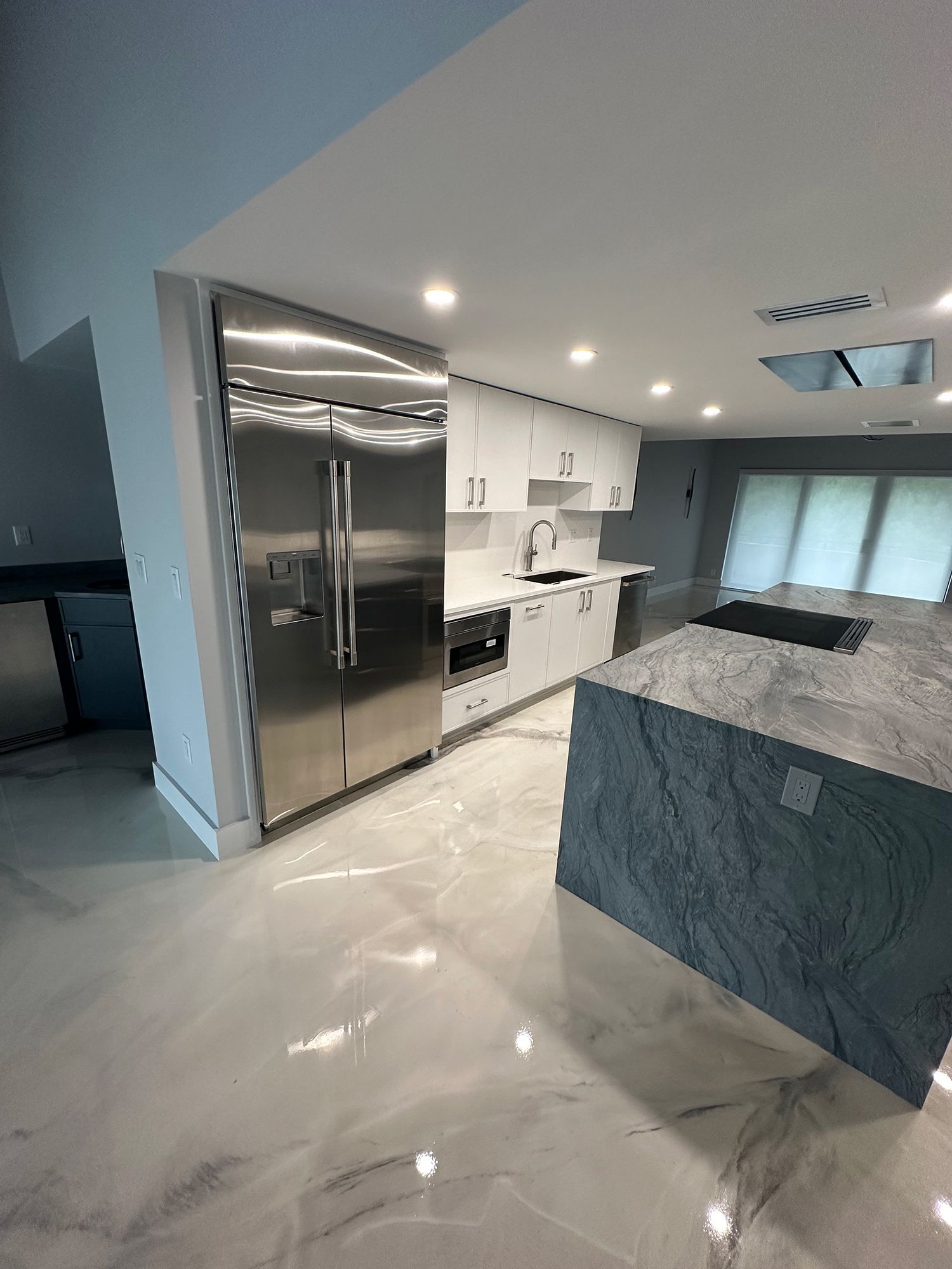 Modern kitchen with white cabinets, stainless steel refrigerator, and gray island with marbled countertop.