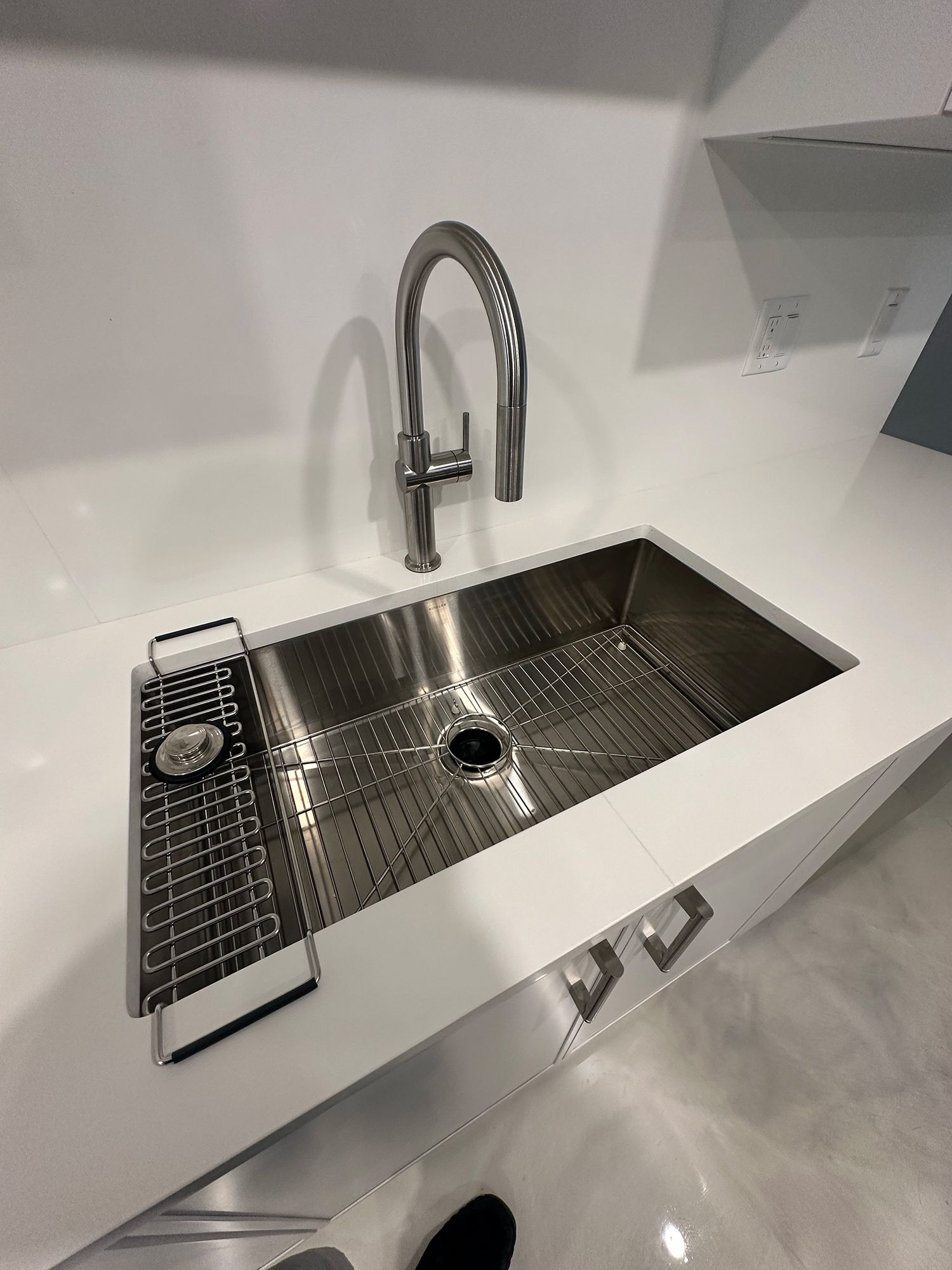 Stainless steel kitchen sink with a faucet and integrated drainer on a white countertop.