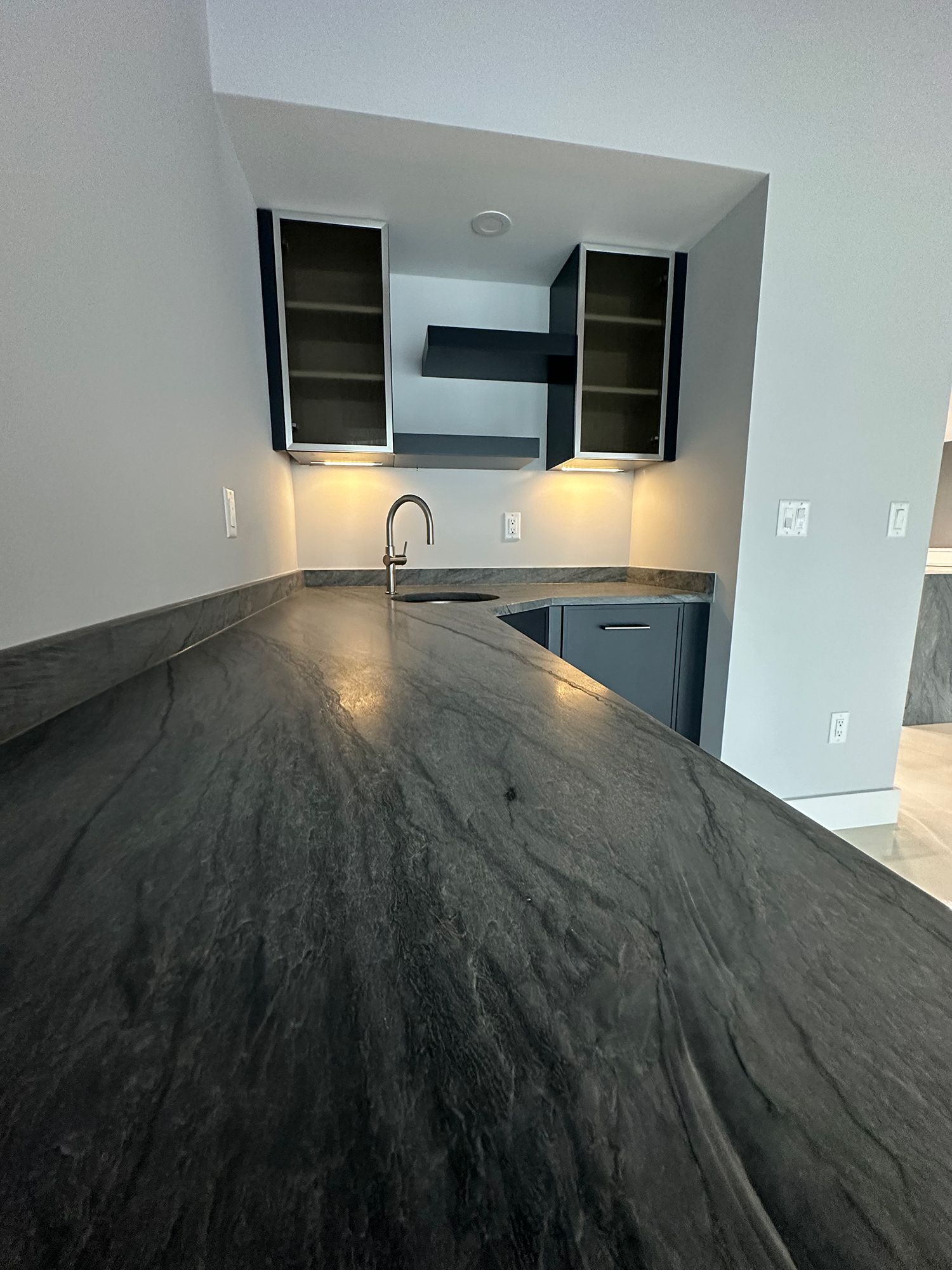 Dark gray countertop with a sink, overhead cabinets, and a vent hood.