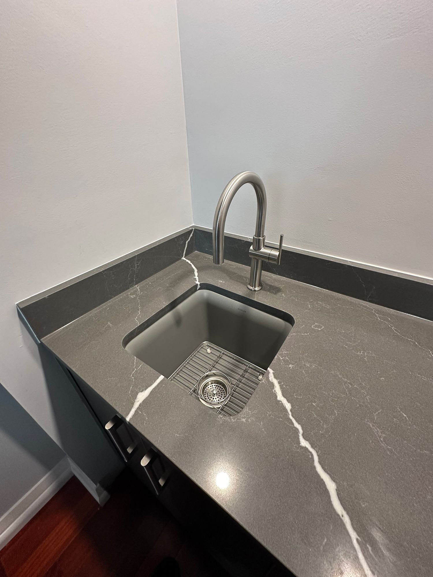 Corner kitchen sink with gray quartz countertop and stainless steel faucet.