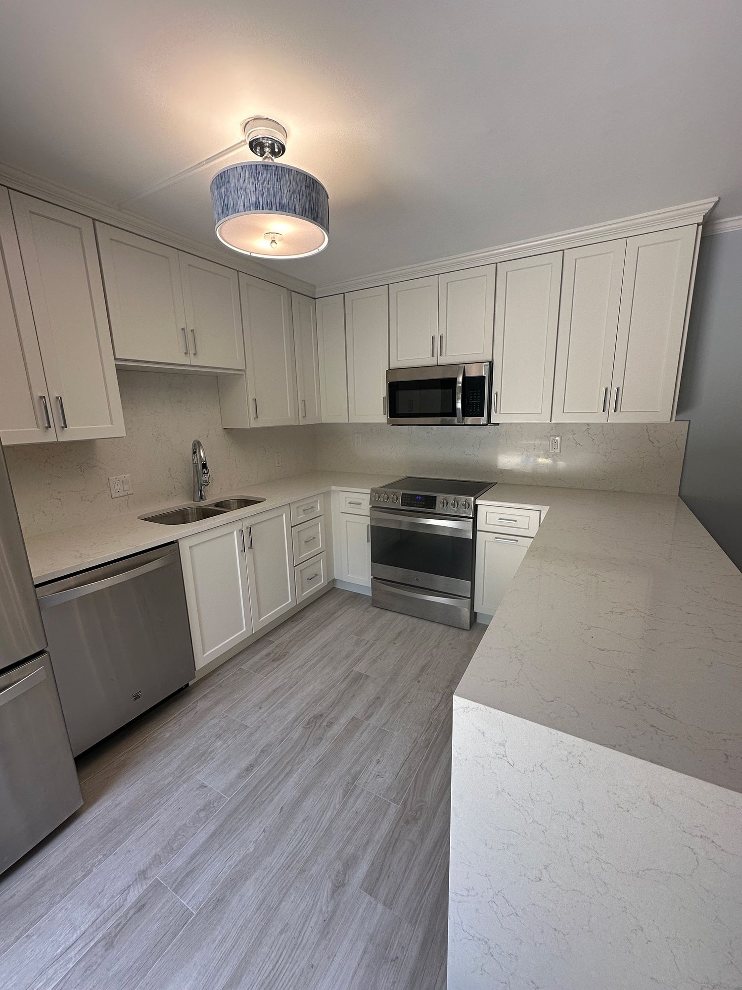 White kitchen with stainless steel appliances, light gray flooring, and quartz countertops.
